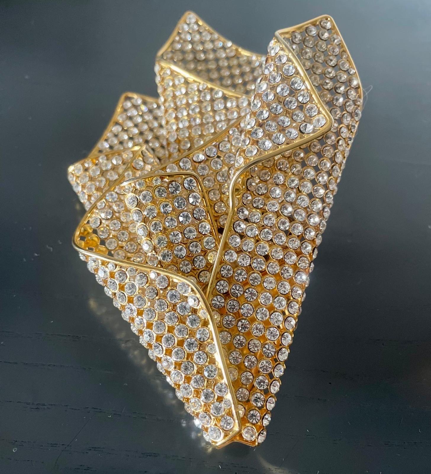 Valentino brooch. 1980s. Shaped like a drape in golden metal and sparkling rhinestones. 
Measurements: 11 cm X 15 cm
Very rare, collectible accessory. Like new, excellent condition.