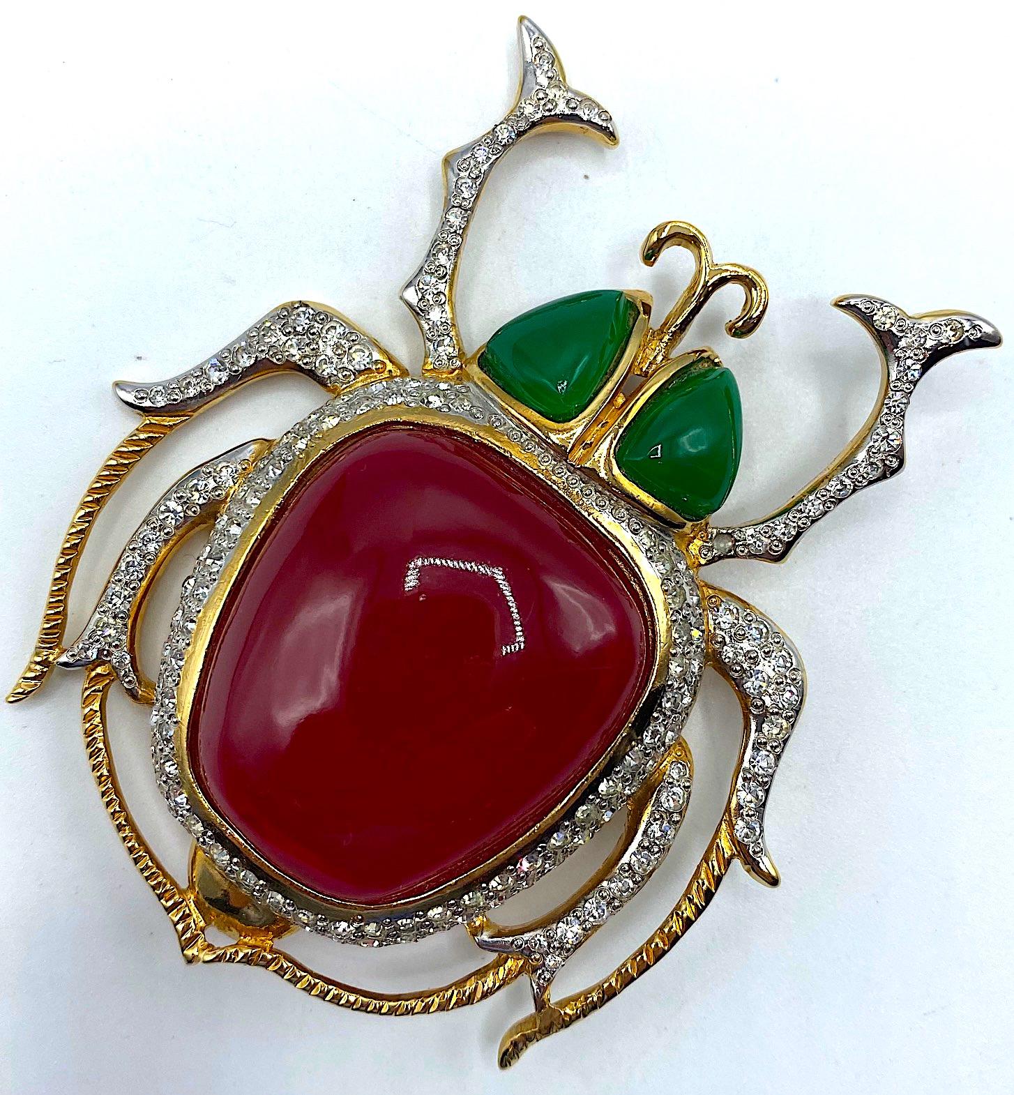 A beautiful and large scarab brooch by famous fashion house Maison Valentino circa 1990. The gold plate brooch is set with rhinestones and green resin molded cabochons for eyes and a large red resin cabochon stone for the body. The brooch measures