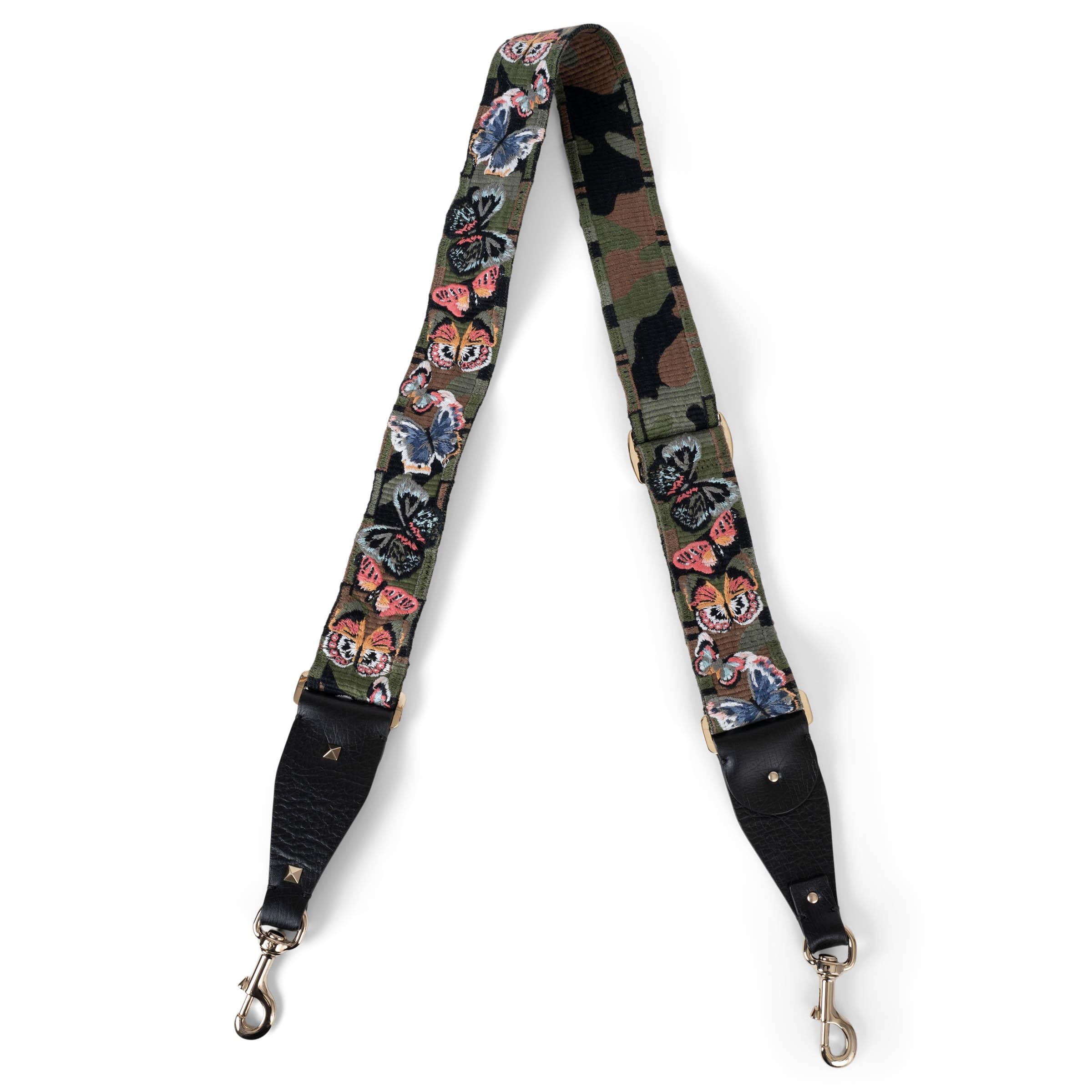 Questa tracolla per borsa Camu Butterfly di Valentino, autentica al 100%, è un mix sorprendente di utilità e artigianalità. Realizzata in tela mimetica verde militare e riccamente ricamata con farfalle multicolore, aggiunge un tocco artistico e