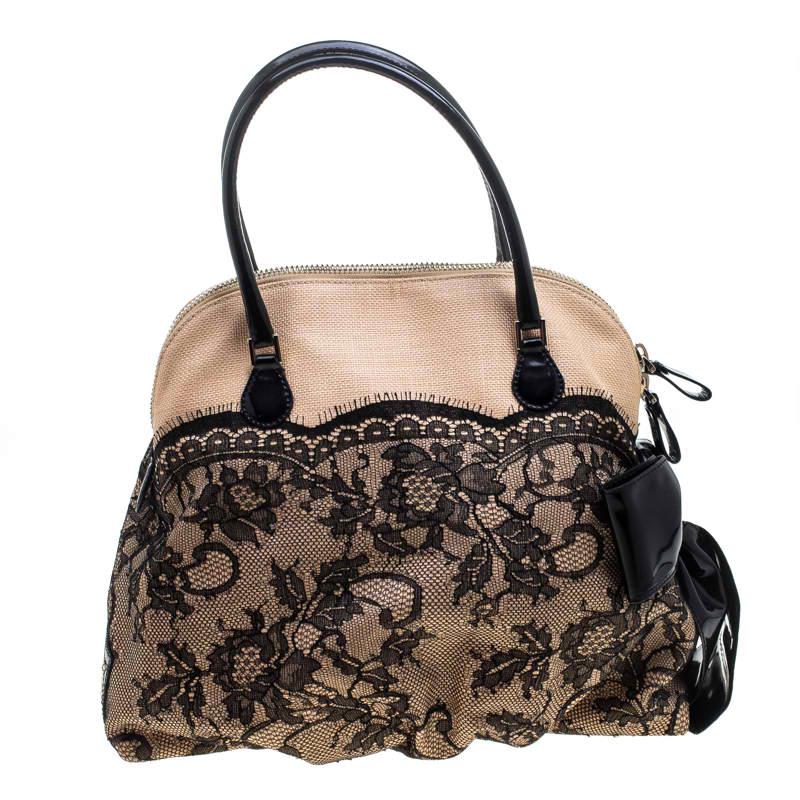 Satchels like these are hard to come by, so quickly grab one when you can! This dome satchel by Valentino is made from canvas and has lace work on the exterior and a black bow fixed on one side. The zip top closure opens to a fabric-lined interior