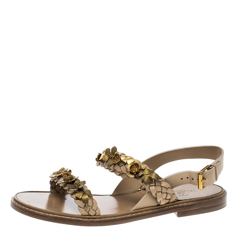 These beige leather sandals are detailed with braided front straps and are beautifully embellished with intricate gold-tone metal flowers arranged on the top. This open toe, small stacked wooden heel comes from the house of Valentino to add glamour