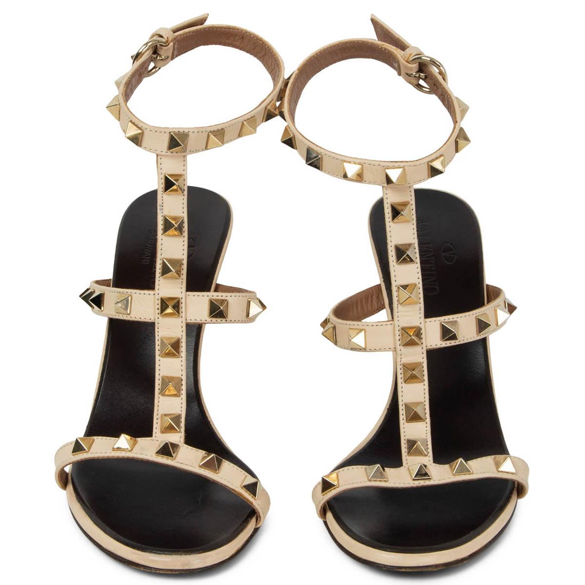 100% autentici sandali Valentino Rockstud con cinturino a T in pelle beige chiaro impreziositi da borchie piramidali in metallo dorato. Sono state indossate e presentano una leggera usura sui tacchi. Nel complesso in ottime condizioni.