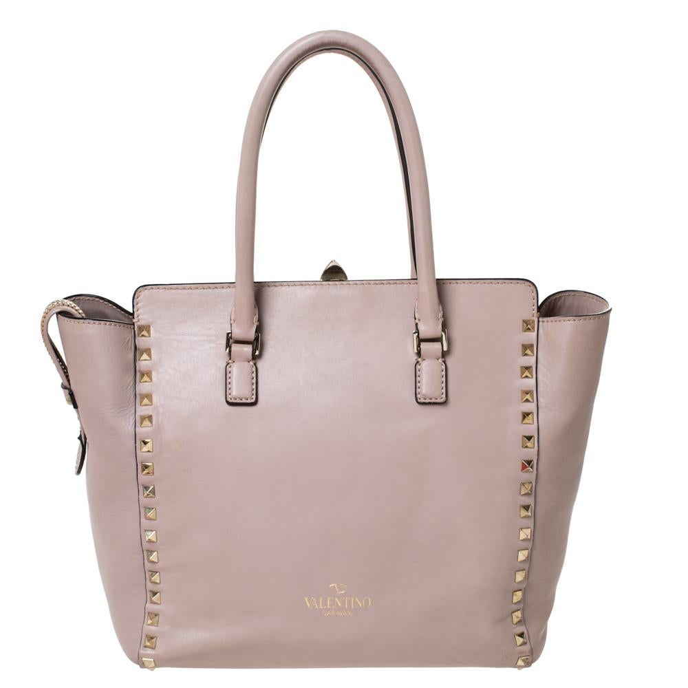 Valentino brings you this super-stylish tote that carries a design which transcends trends. It has a beige leather exterior decorated with the signature pyramid Rockstuds. The tote is complete with a spacious canvas interior, two top handles and a