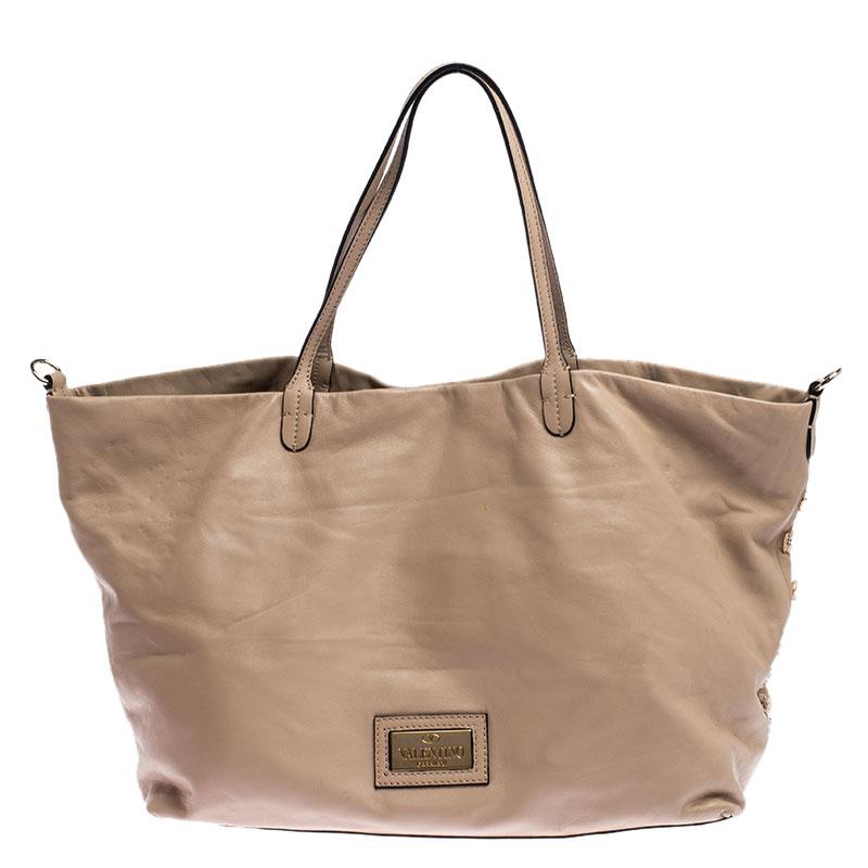 This gorgeous tote from Valentino is crafted from beige leather and features stunning sequin and beaded floral embellishment. The bag comes with dual handles and protective metal feet at the bottom. It has a spacious satin-lined interior that houses