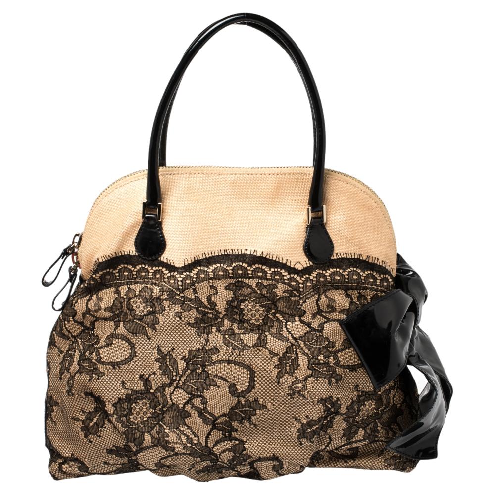 This Dome bag by Valentino will make a fashion-forward statement. Crafted from lace and woven straw, it is highlighted with a patent leather bow detailing on the side along with dual top handles. The zip-enclosed fabric-lined interior houses a