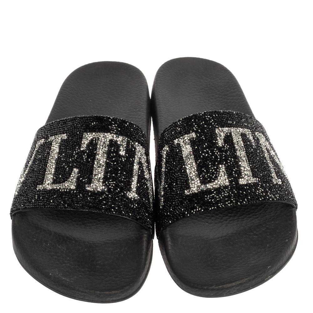 Comfort and luxe fashion come combined in these slides from Valentino! They are designed with a rubber base and the VLTN logo on the crystal-covered uppers. The black slides are made for you to lounge around in style.

