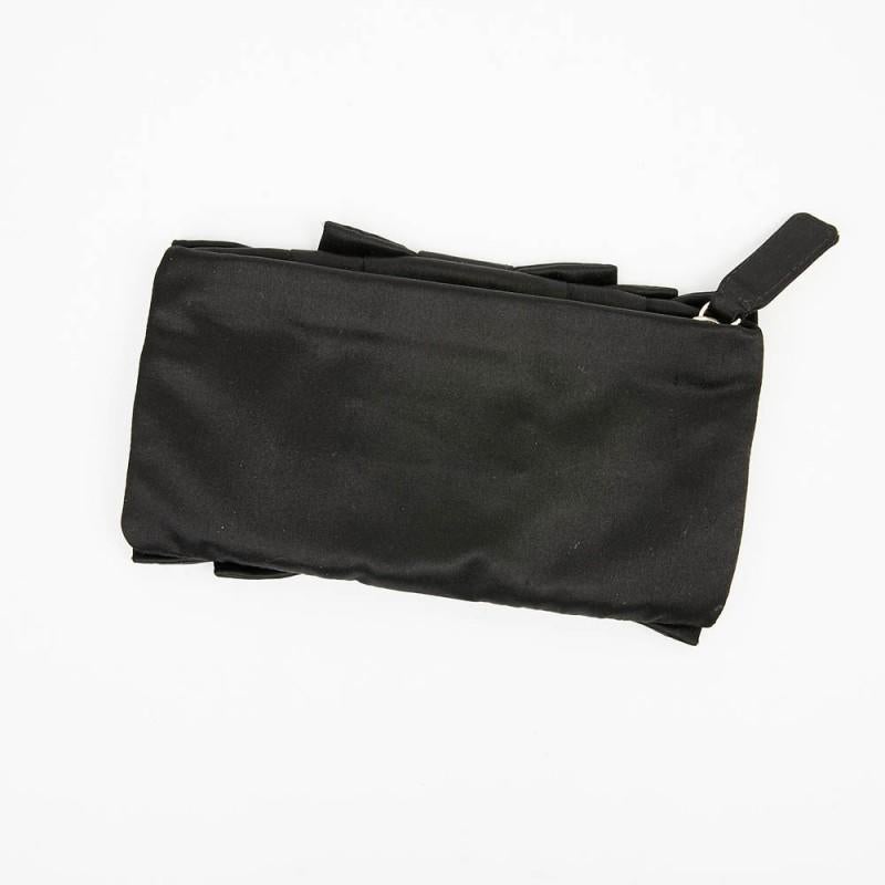 This small evening pouch Garavani VALENTINO is in black satin with a rectangular shape. A knot on the front make by the pleating, it is smooth on the back. The jewelry is gilt metal and it closes with a zipper. It is lined with black silk and you