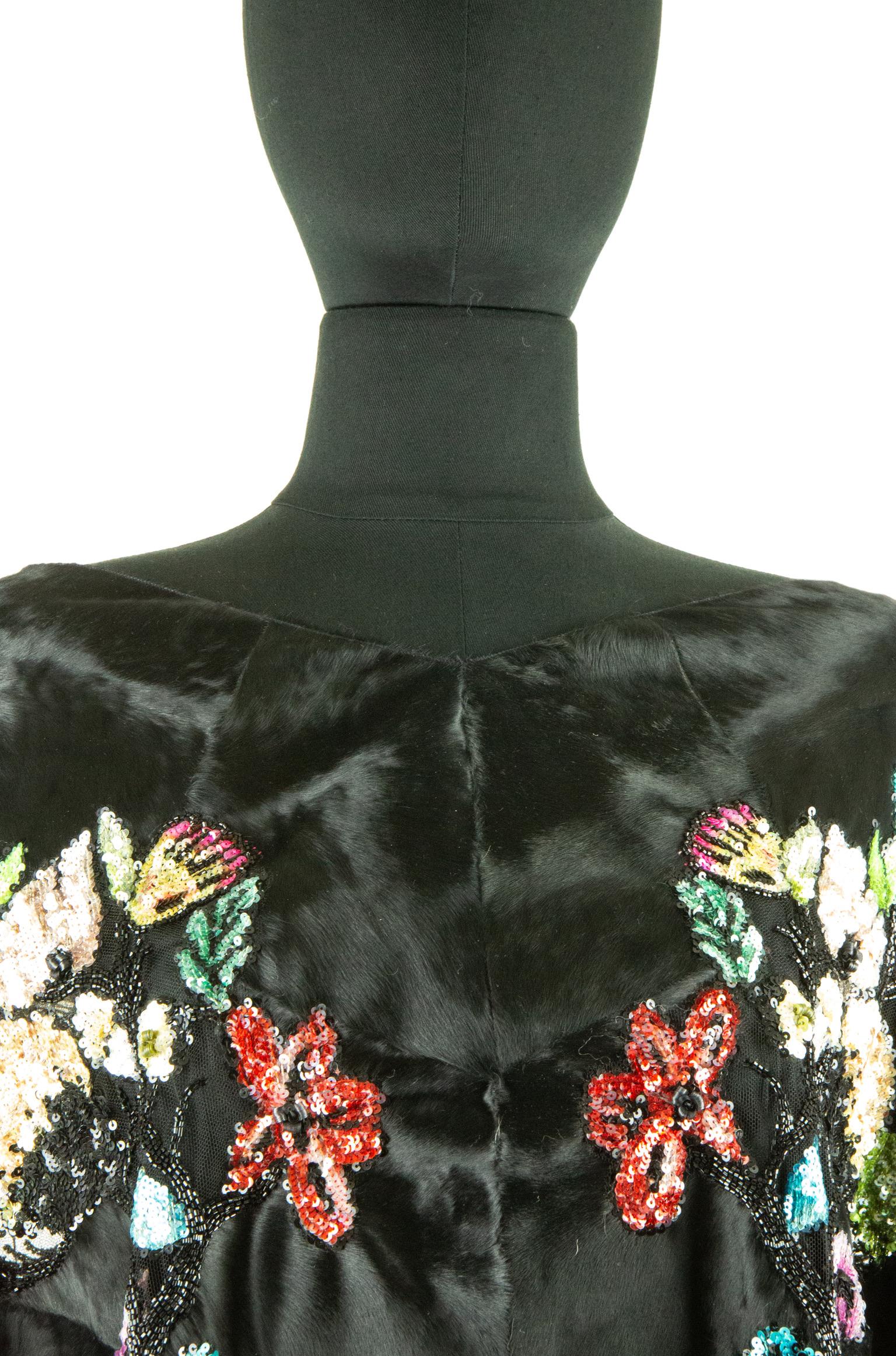 This Valentino shawl is made from Broadtail dyed lambs’ fur and features an all-over glass beaded embroidery of an assortment of flowers in a range of bright colours. The shawl has a wide neckline and mid-length sleeves and falls just below the