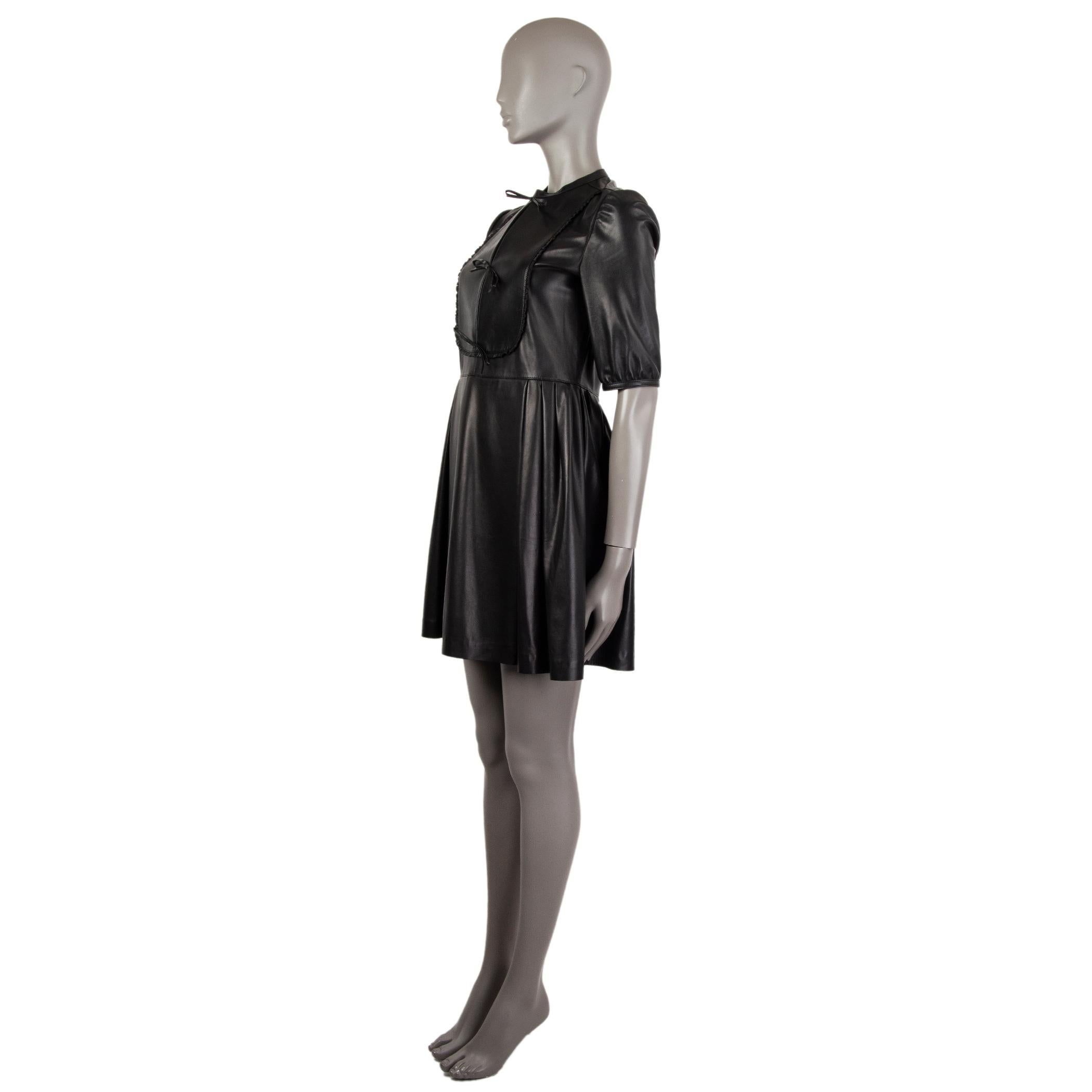 Valentino 3/4-sleeve dress in black lambskin. With keyhole neck tied with three leasther bows, ruffle-trim bib, pleated skirt, and one-button narrow cuffs. Closes with button and concealed zipper on the back. Unlined. Has been worn and is in