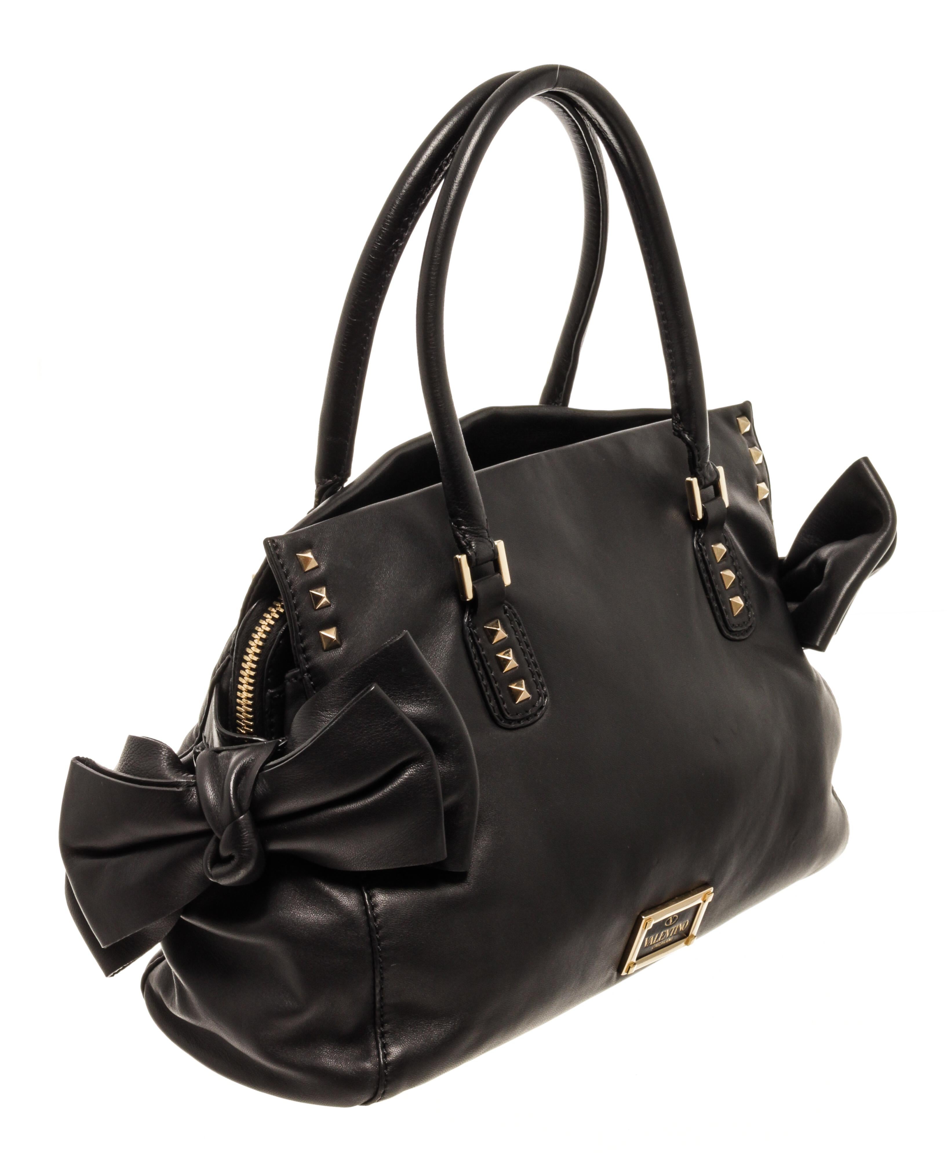Valentino Black Leather Bow Convertible Handbag with gold-tone hardware, gold-tone metal bag foot, exterior rockstuds accents , exterior gold-tone Valentino embossed logo, two bows at both sides black interior lining, three compartments with one