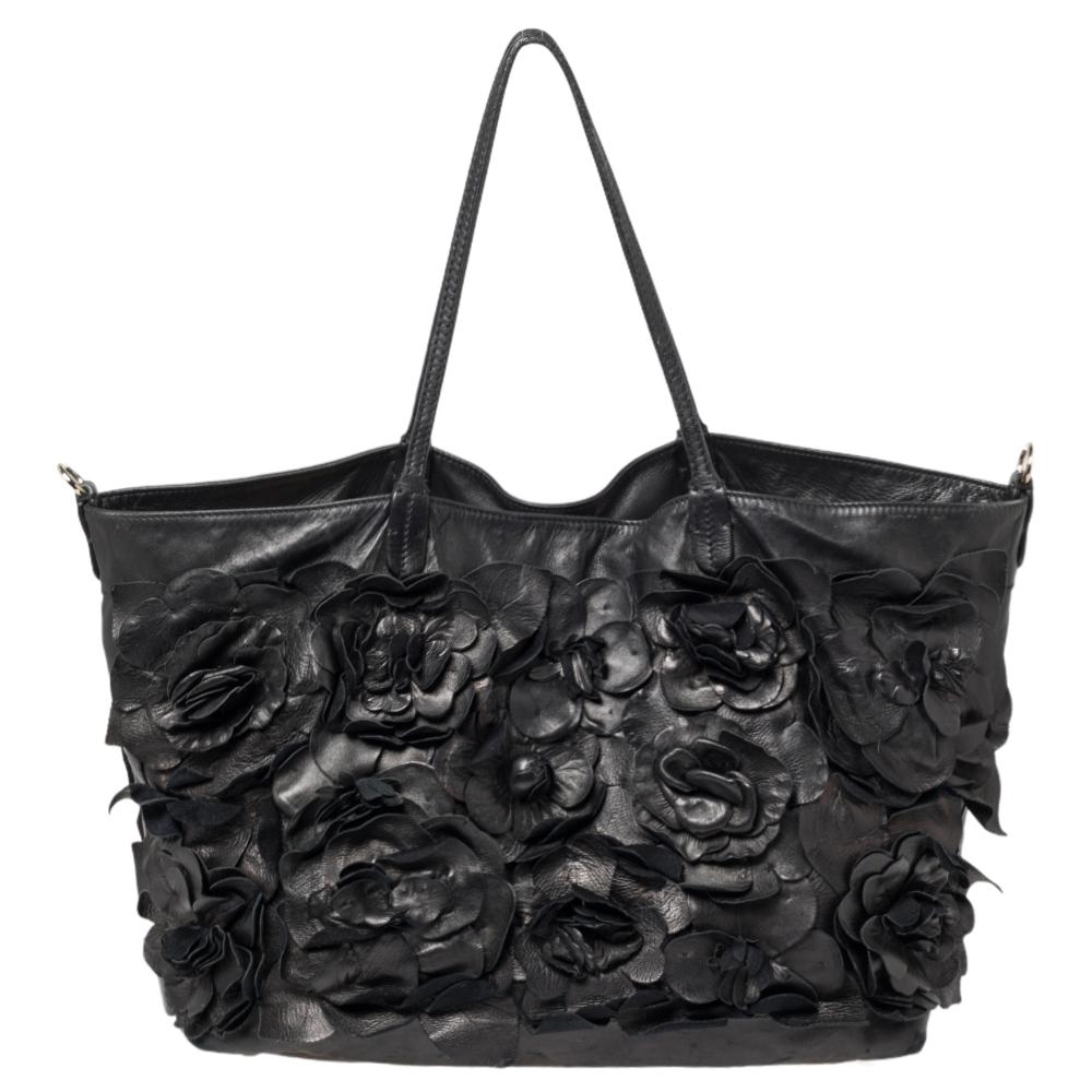 Valentino is known to bring out unique and one-of-a-kind pieces year after year and this tote are indeed one of them! It is crafted beautifully from black leather with flower appliques on the front and a brand label plaque on the side. It comes