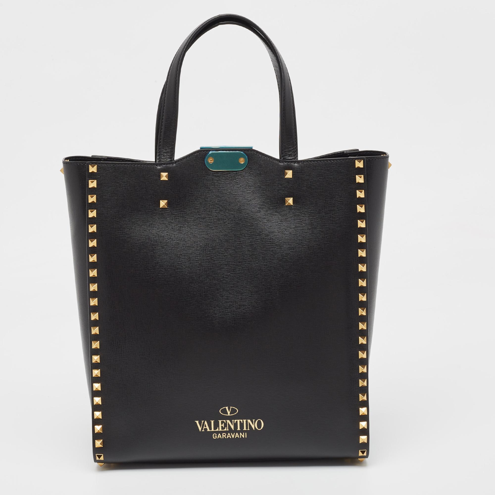 This Alcove tote from Valentino is a perfect blend of function and style. It features a black leather construction enhanced with dual top handles, a detachable strap, and gold-tone Rockstud accents. It is equipped with a spacious interior to easily