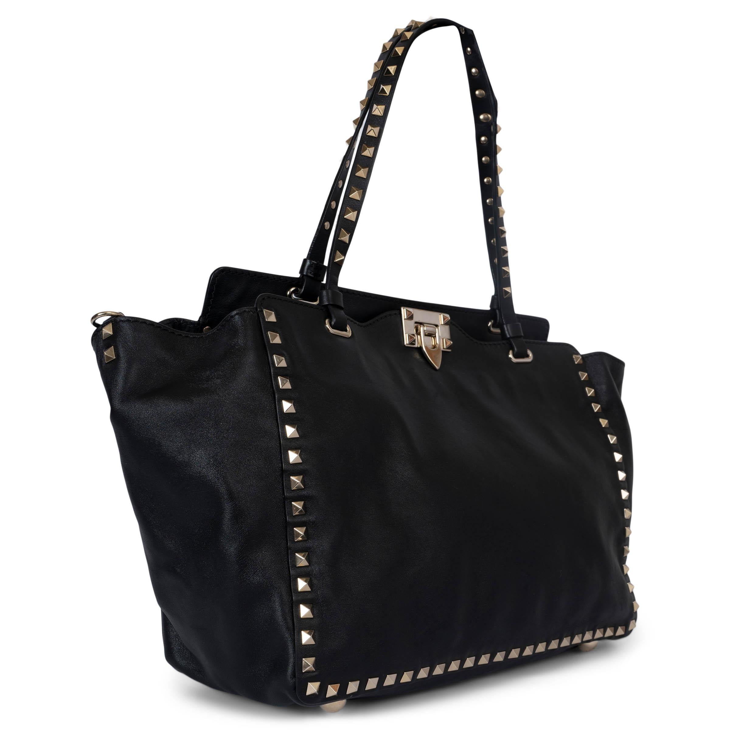 100% authentic Valentino Medium Rockstud Trapeze shoulder bag in black calfskin featuring signature patinum-finish rockstuds in light gold-tone metal. Lined in black canvas with one zipper pocket against the back and two open pockets attached. Comes