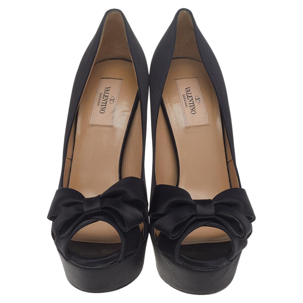 Add a luxe finish to your outfit with these Valentino platform pumps. They are crafted from black satin and designed with bows, peep toes, platforms, and 14 cm heels.

