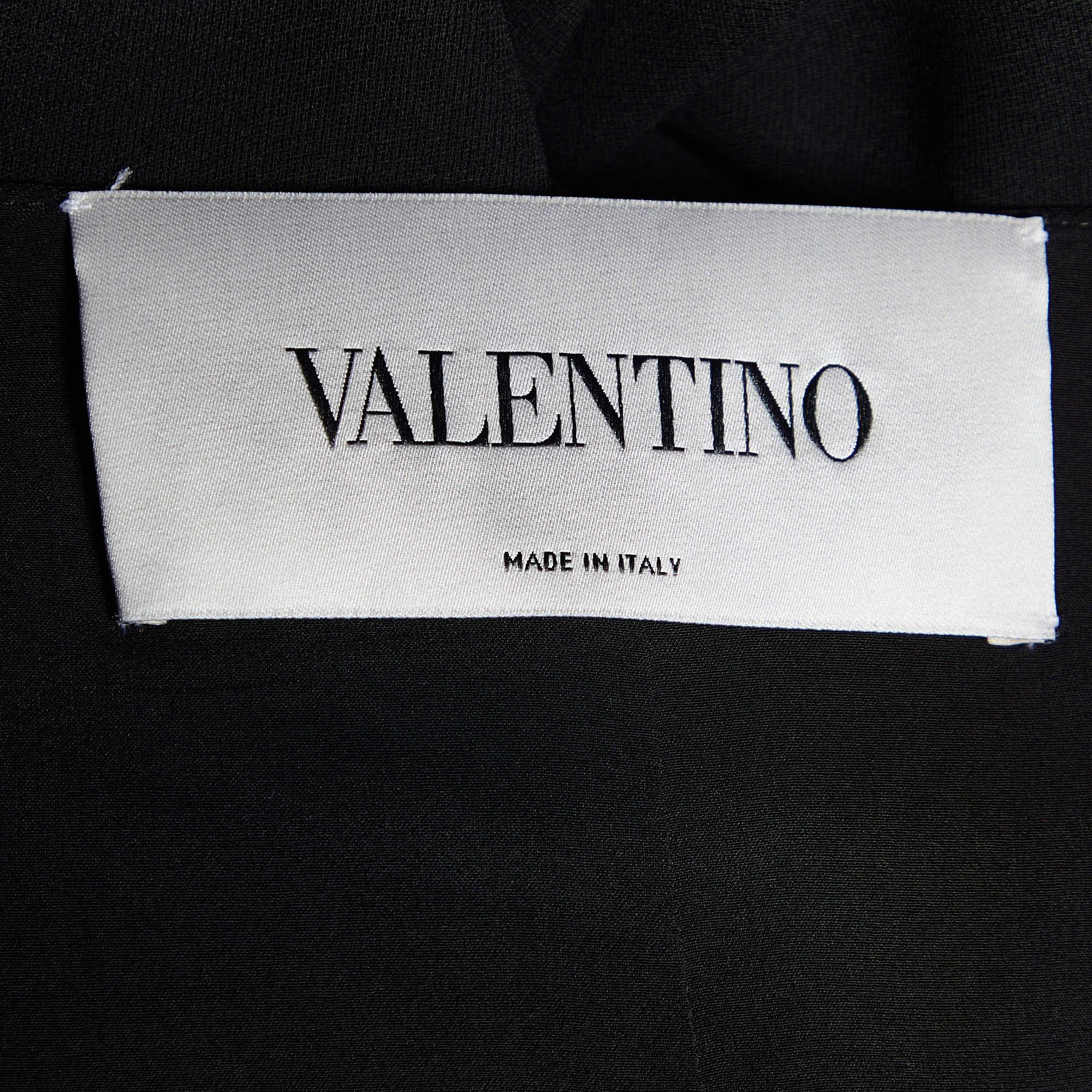 Confectionnée en crêpe de soie noir somptueux, cette robe longue sans manches signée Valentino respire l'élégance intemporelle. Sa silhouette fluide se drape gracieusement, accentuant chacun de vos mouvements. Le décolleté plongeant ajoute une