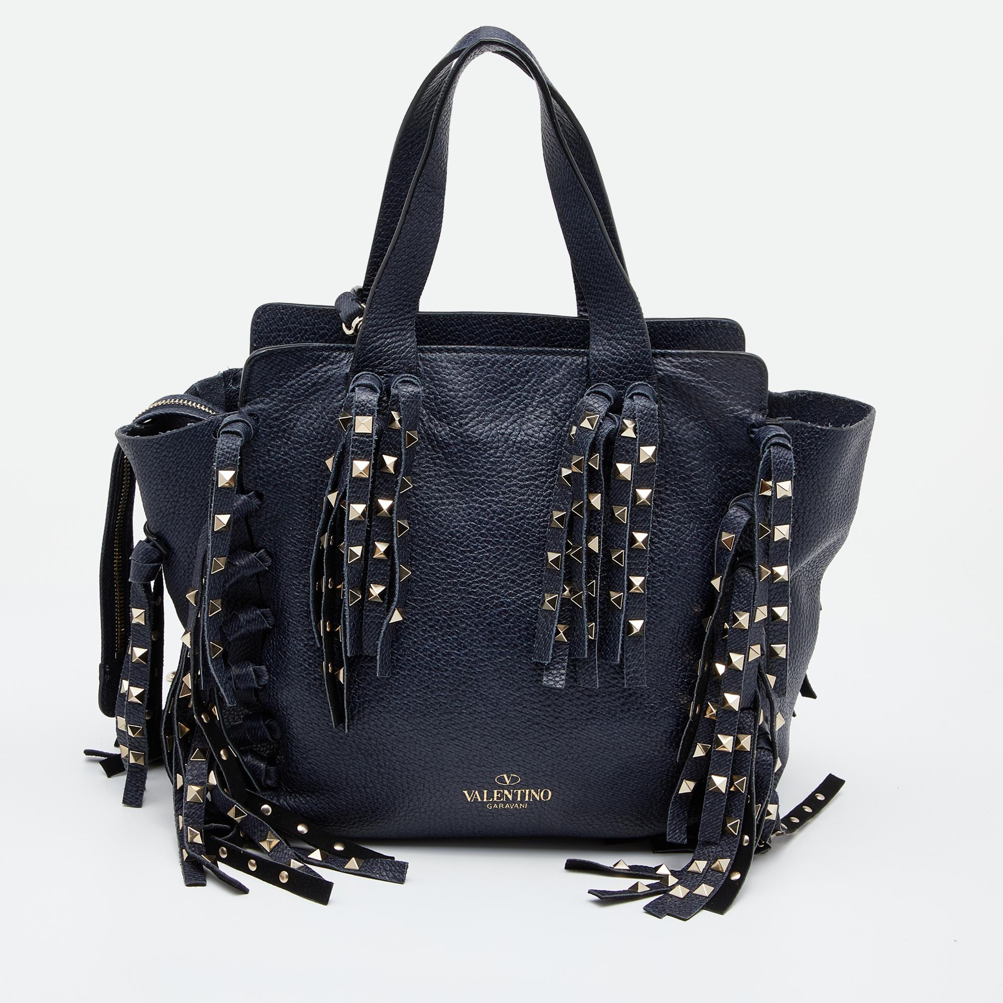 Every modern-day wardrobe needs a Valentino tote like this. Get this beautiful leather bag featuring a lovely touch of fringe details covered with the signature Rockstuds. It is complete with a capacious interior that can easily house your