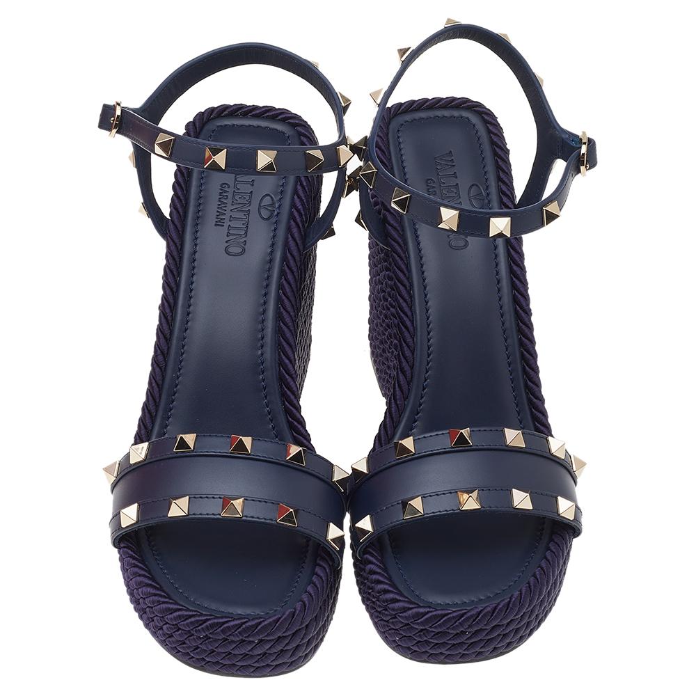 Complete a chic look with this pair of Valentino wedge sandals. Constructed using blue leather, the open-toe sandals are embellished with Rockstud motifs, secured with buckle closure at the ankles, and lifted on espadrille wedge heels.