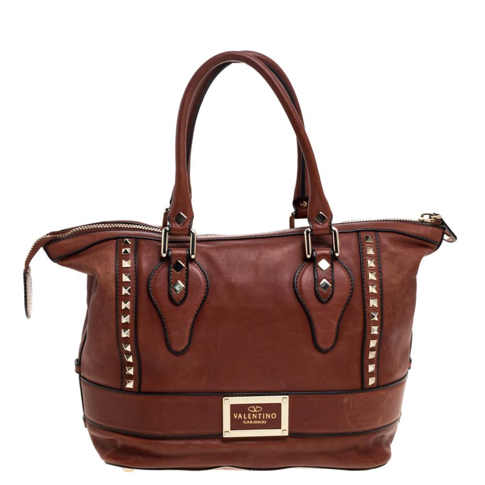 This brown leather tote from Valentino is classic and elegant. With gold-tone Rockstuds, bow detail to the front, and the brand label at the rear, this tote features a wonderful exterior. Fully lined with satin, the spacious interior has one zip and