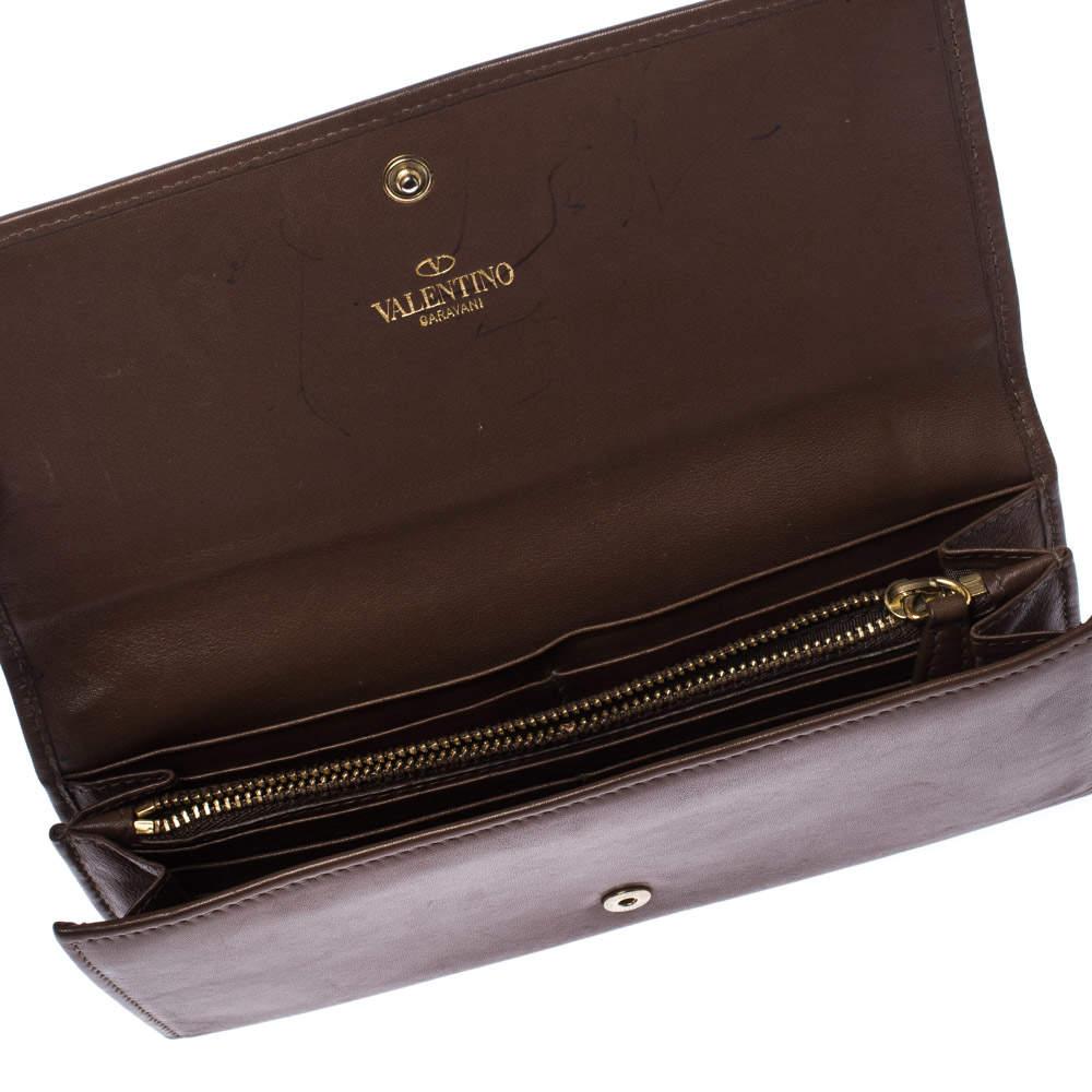 Carry your bills and cards in this Valentino wallet. The brown leather exterior is accented with gold-tone V-ring motif. The flap closure opens to a leather and fabric-lined interior. The interior houses multiple card slots and a zipper pocket.