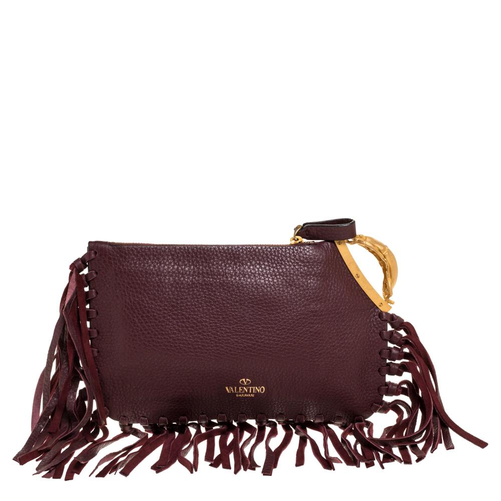 Glamor is redefined with this exquisite C Rockee clutch from Valentino. Crafted with luxe leather, this clutch is accented with knotted fringes along its edges, and a gold-tone gryphon detail. The suede-lined interior is secured by a zip