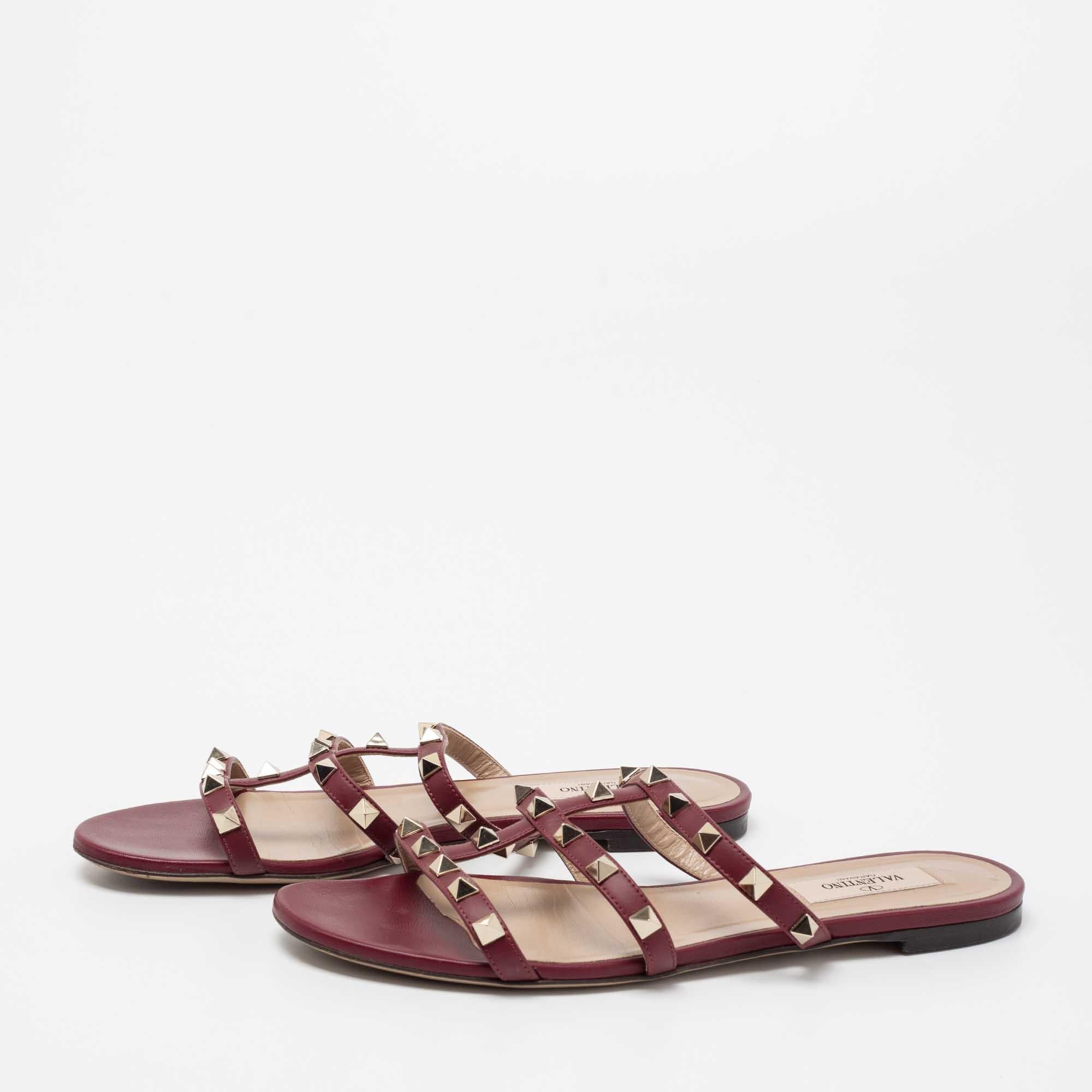 Lend your feet comfort, signature beauty, and luxury with these stunning slide sandals from Valentino. They are crafted using burgundy leather, with Rockstud embellishments perched on the upper. They flaunt gold-tone hardware and a slip-on style.