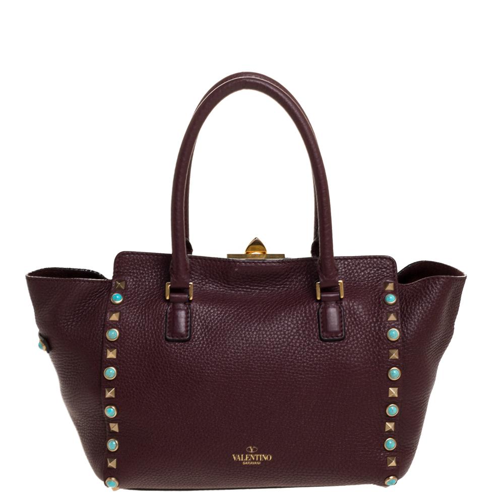 Valentino brings you this super-stylish tote that carries a design that will surely grab the attention of your onlookers. It has a burgundy leather exterior decorated with the signature pyramid Rockstuds. The tote is complete with a spacious suede