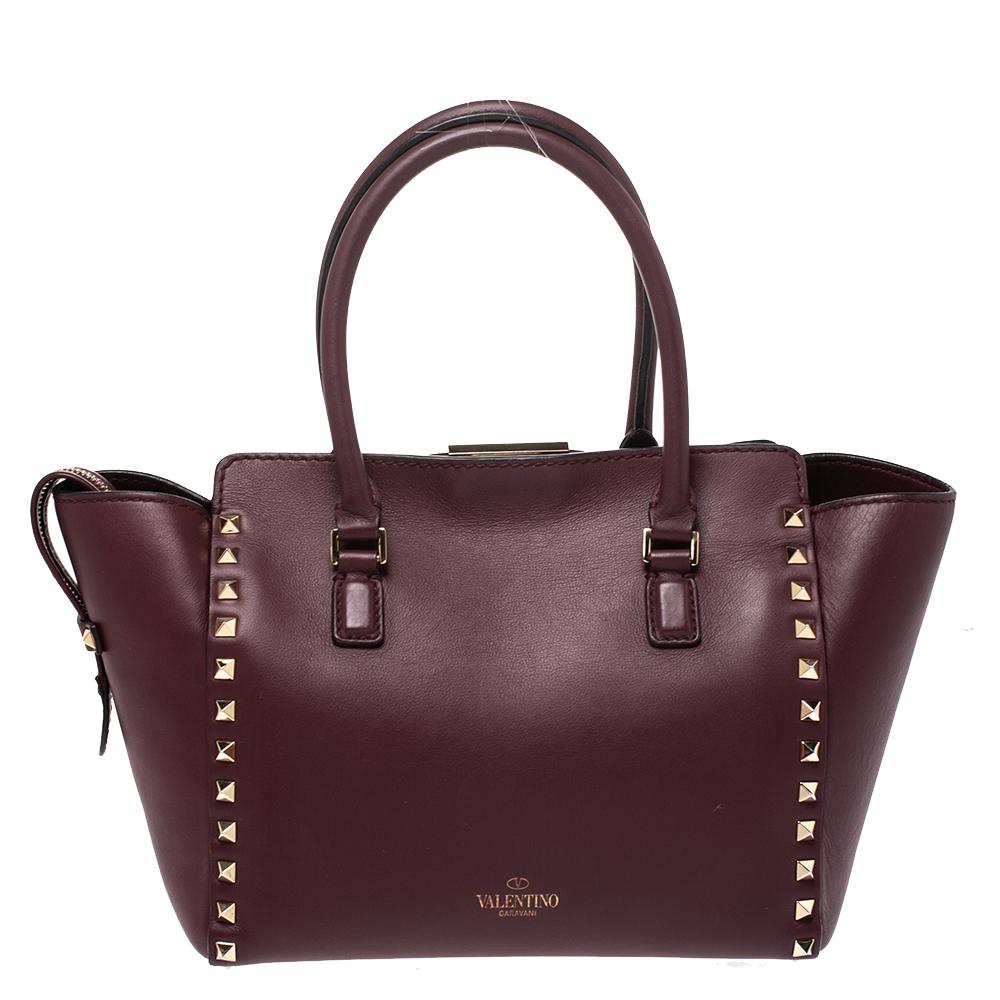 Valentino brings you this super-stylish tote that carries a design which will surely grab the attention of your onlookers. It has a burgundy leather exterior decorated with the signature pyramid Rockstuds in gold-tone. The tote is complete with a