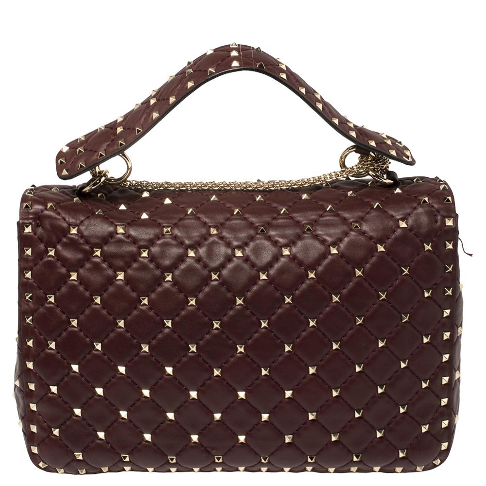 Catch admiring glances when you carry this Rockstud Spike bag from Valentino! Crafted well, the burgundy bag has a top handle, a chain shoulder sling and it features the iconic Rockstuds on the quilted leather exterior. The front flap opens to a