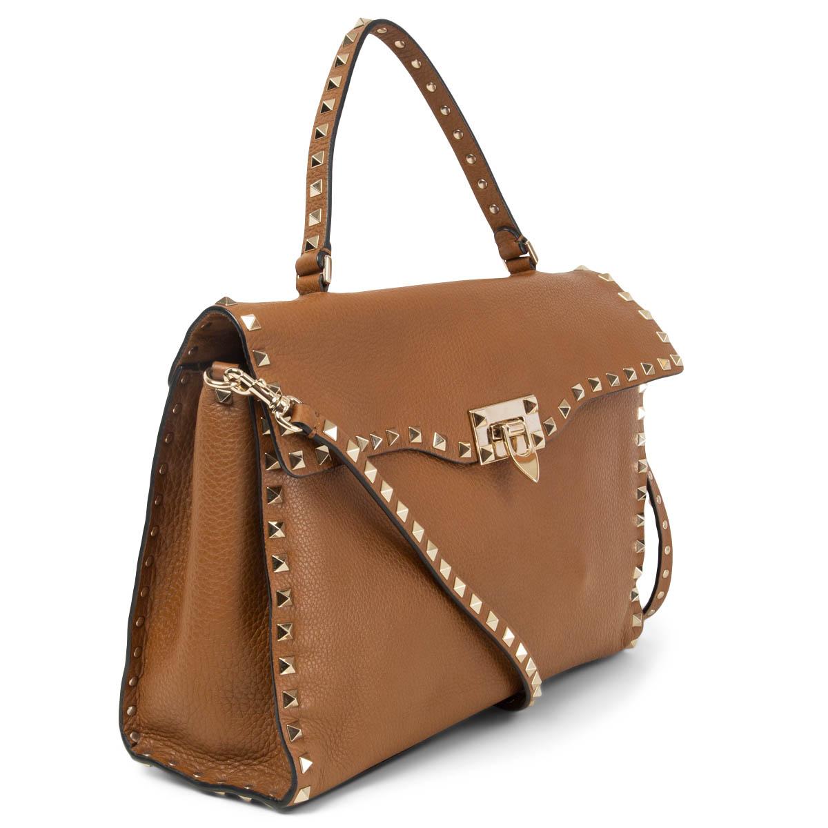 100% authentic Valentino Garavani Medium Rockstud top-handle bag in grainy brown calfskin featuring platinum-finish metal studs and hardware. Opens with a hook closure and is unlined and divided in two compartments with one big zipper pocket in the