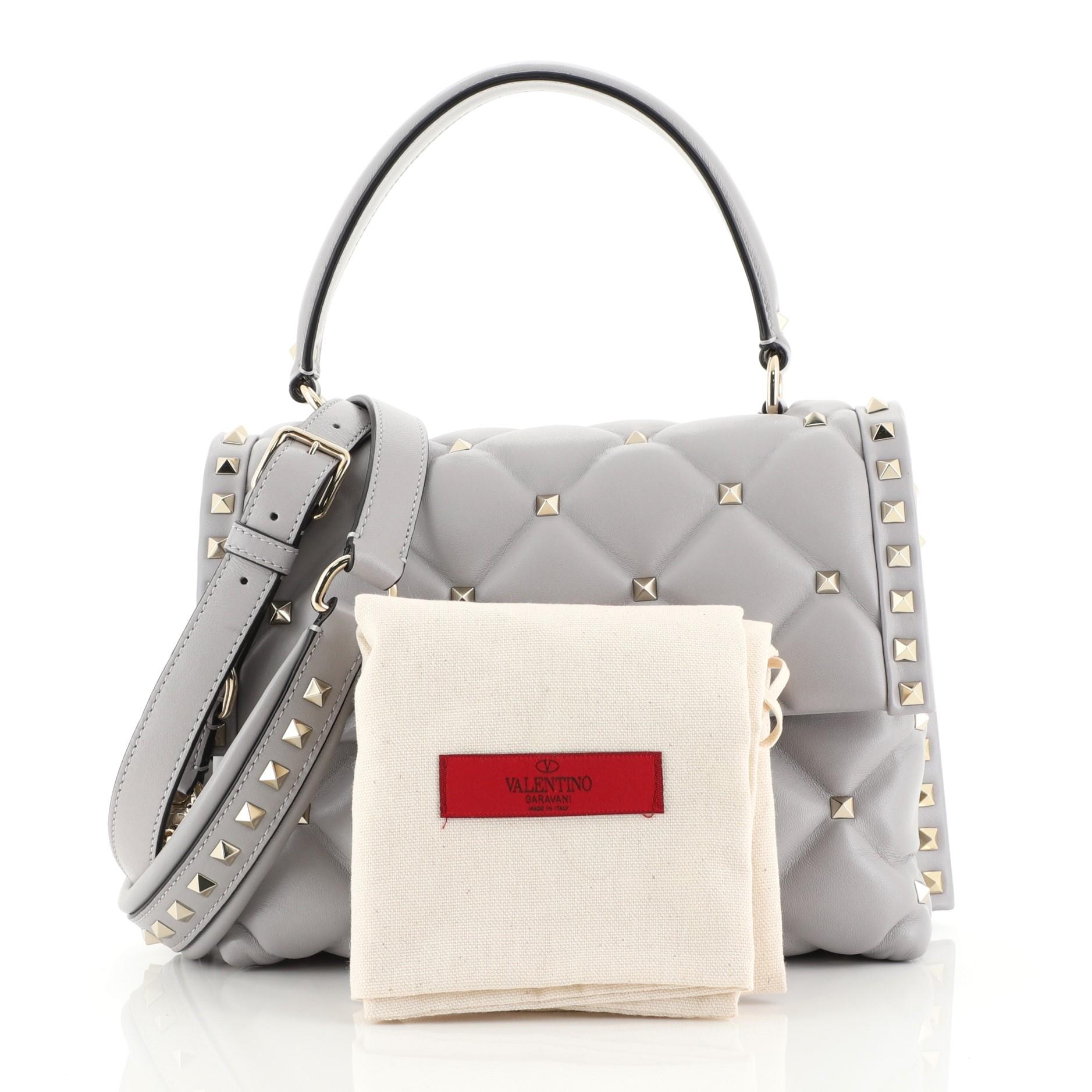 This Valentino Candystud Top Handle Bag Leather Medium, crafted in gray leather, features a leather top handle, rockstud embellishments, and gold-tone hardware. Its twist-lock closure opens to a neutral fabric interior with zip and slip pockets.