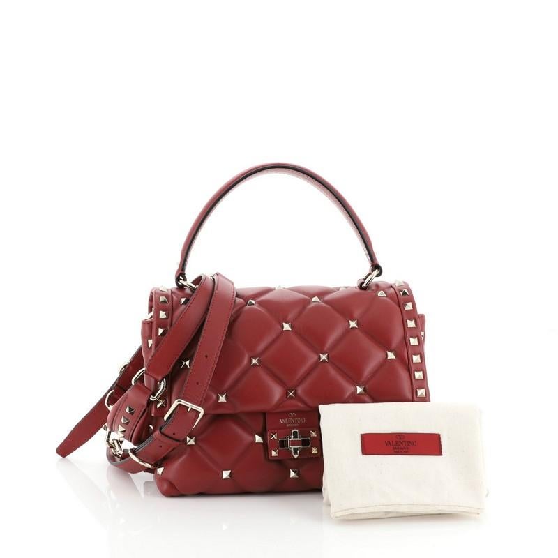 This Valentino Candystud Top Handle Bag Leather Medium, crafted in red leather, features a leather top handle, rockstud embellishments, and gold-tone hardware. Its twist-lock closure opens to a neutral fabric interior with zip and slip pockets.