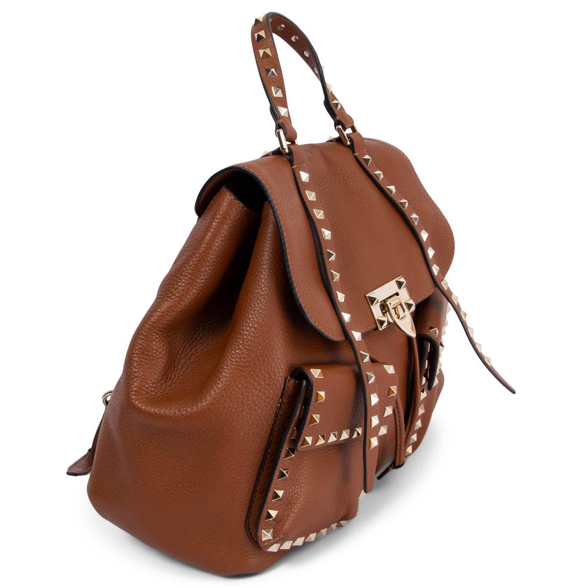 100% authentique Valentino Rockstud Double Pocket Backpack sac à dos en cuir de veau velouté cognac avec clous pyramidaux de couleur or clair qui bordent le sac. Il comporte deux poches frontales à fermeture éclair, des bretelles réglables et un