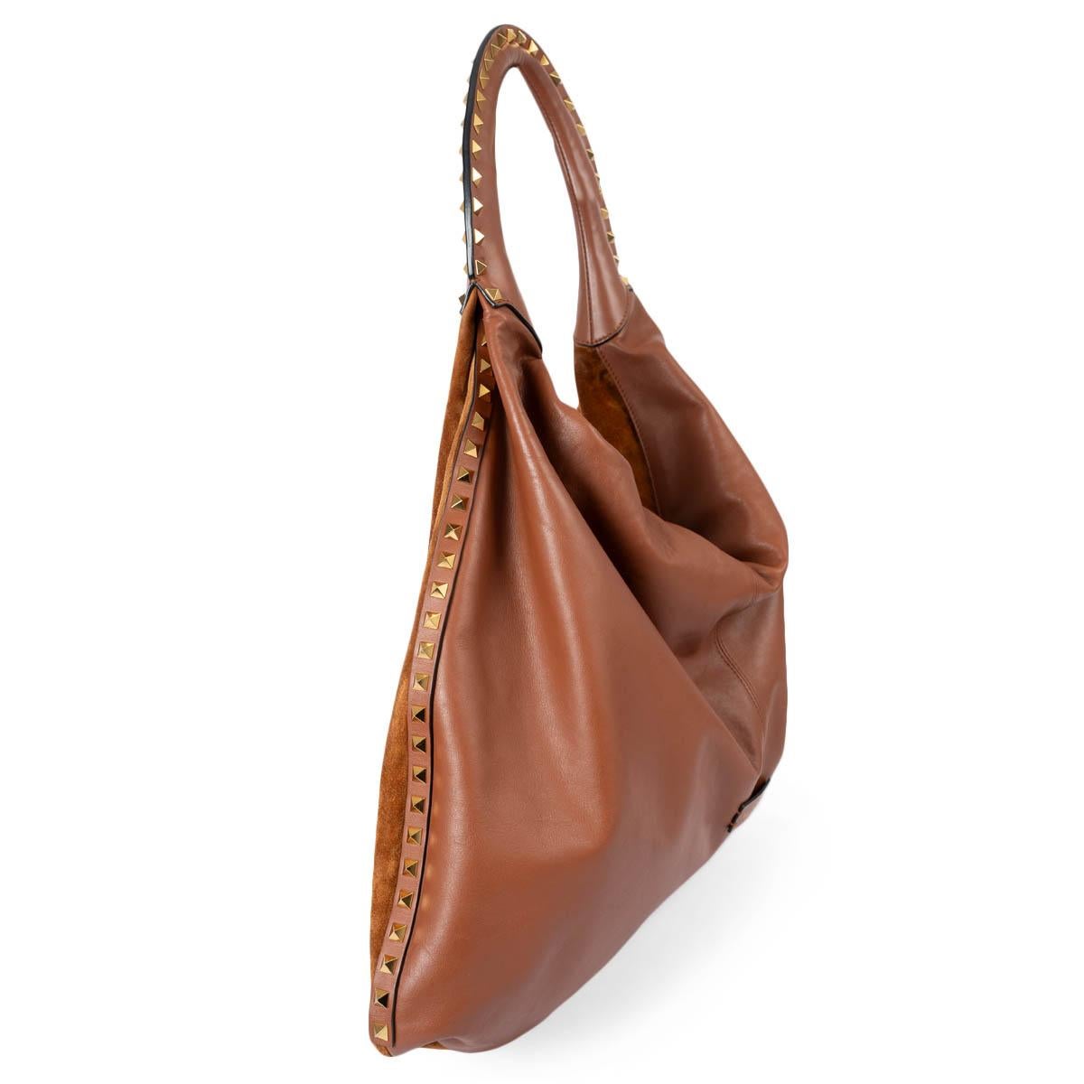 100% authentic Valentino Rockstud hobo in cognac brown suede and leather. Features gold-tone pyramid studs along the handle and gusset and logo patch on the front. Opens with a magnet on top and is lined in black leather with detachable red zipper