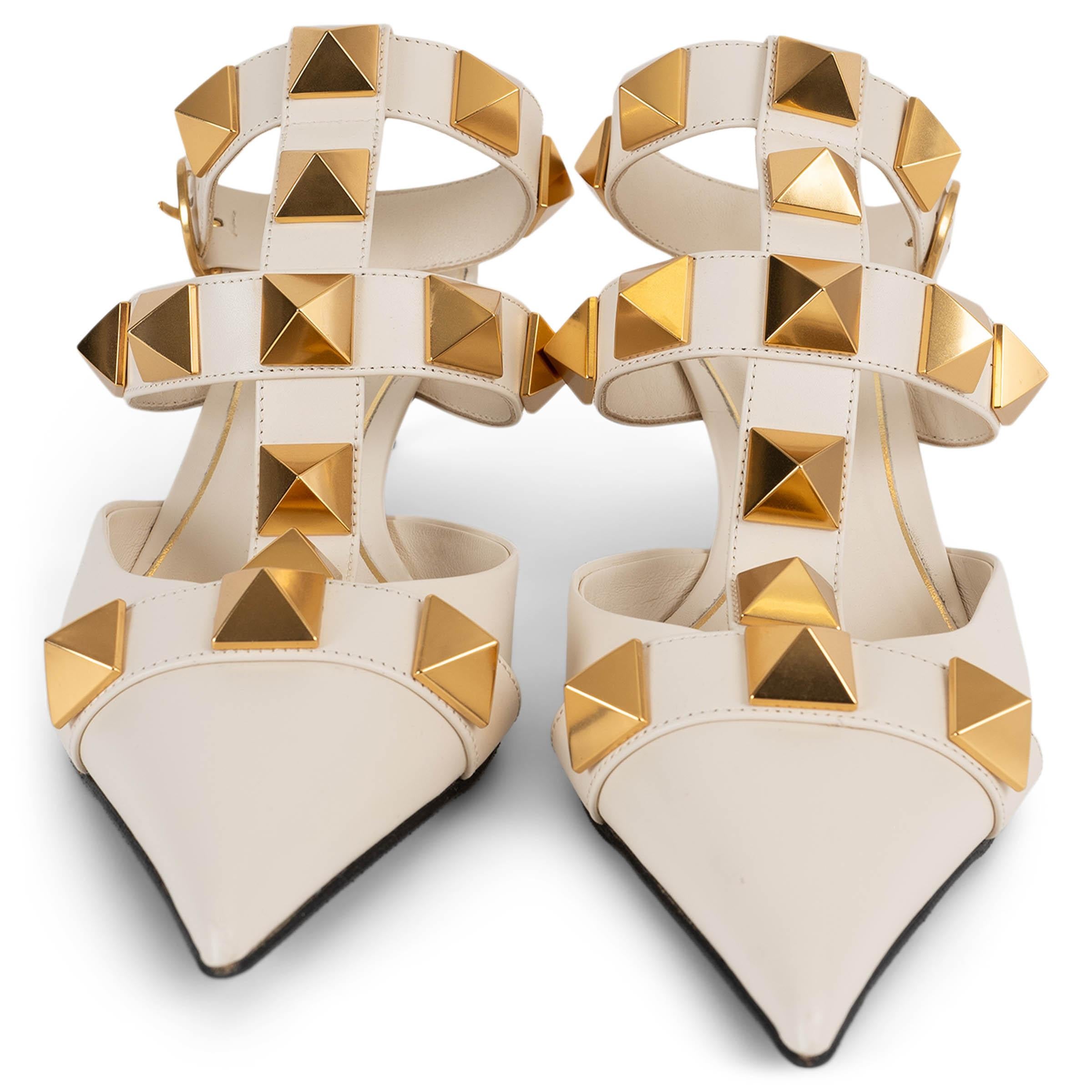 Estas sandalias Roman Stud 100% auténticas de Valentino están confeccionadas en piel color crema y adornadas con las características tachuelas piramidales doradas de gran tamaño. El diseño presenta una puntera puntiaguda y tiras en forma de jaula