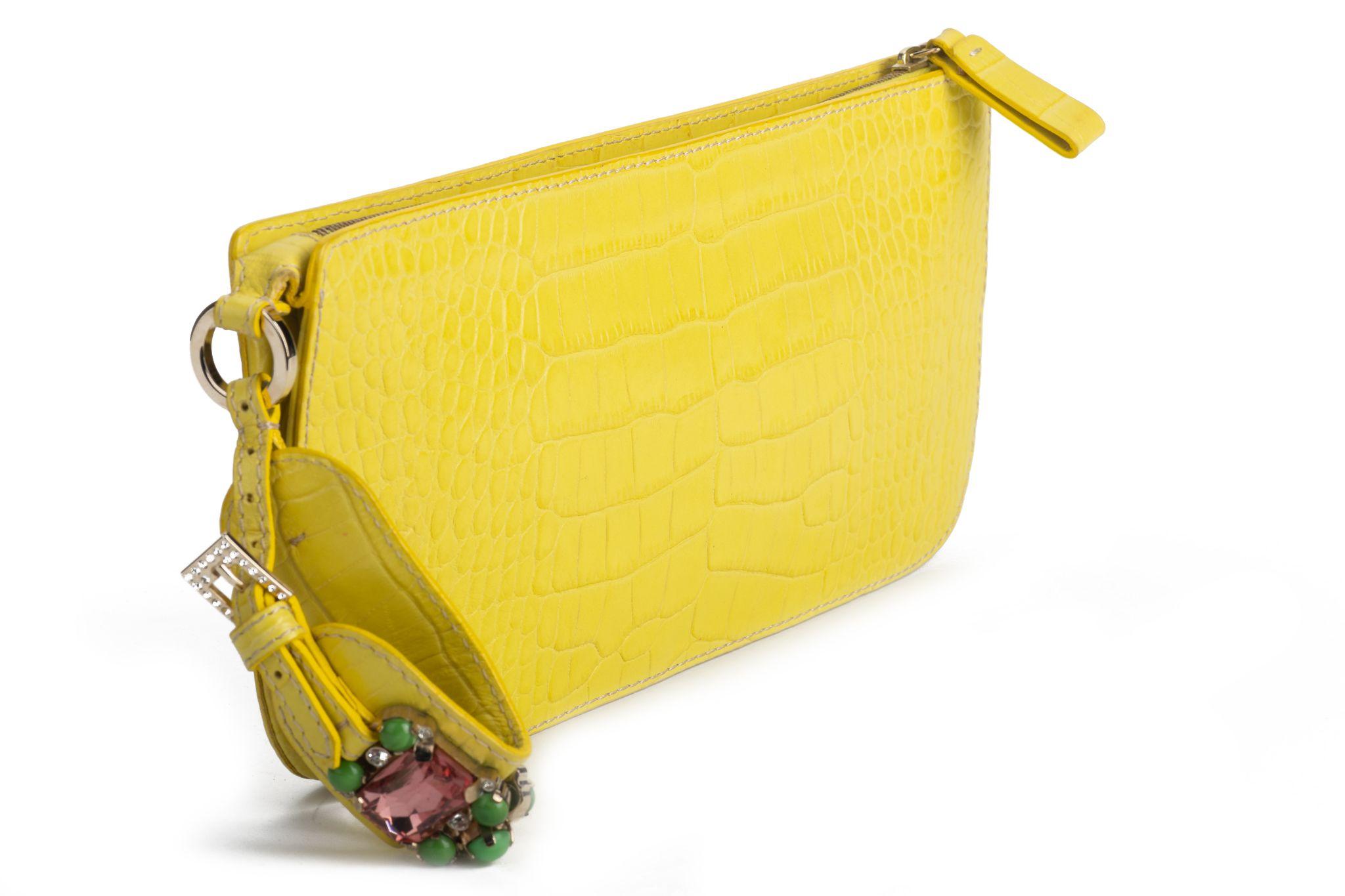 Valentino wrist purse in a vibrant yellow. The leather has a crocodile skin pattern. The wrist band is decorated with multiple stones in different colors and is adjustable. The interior is made of fabric and the Valentino logo is stitched in it. The