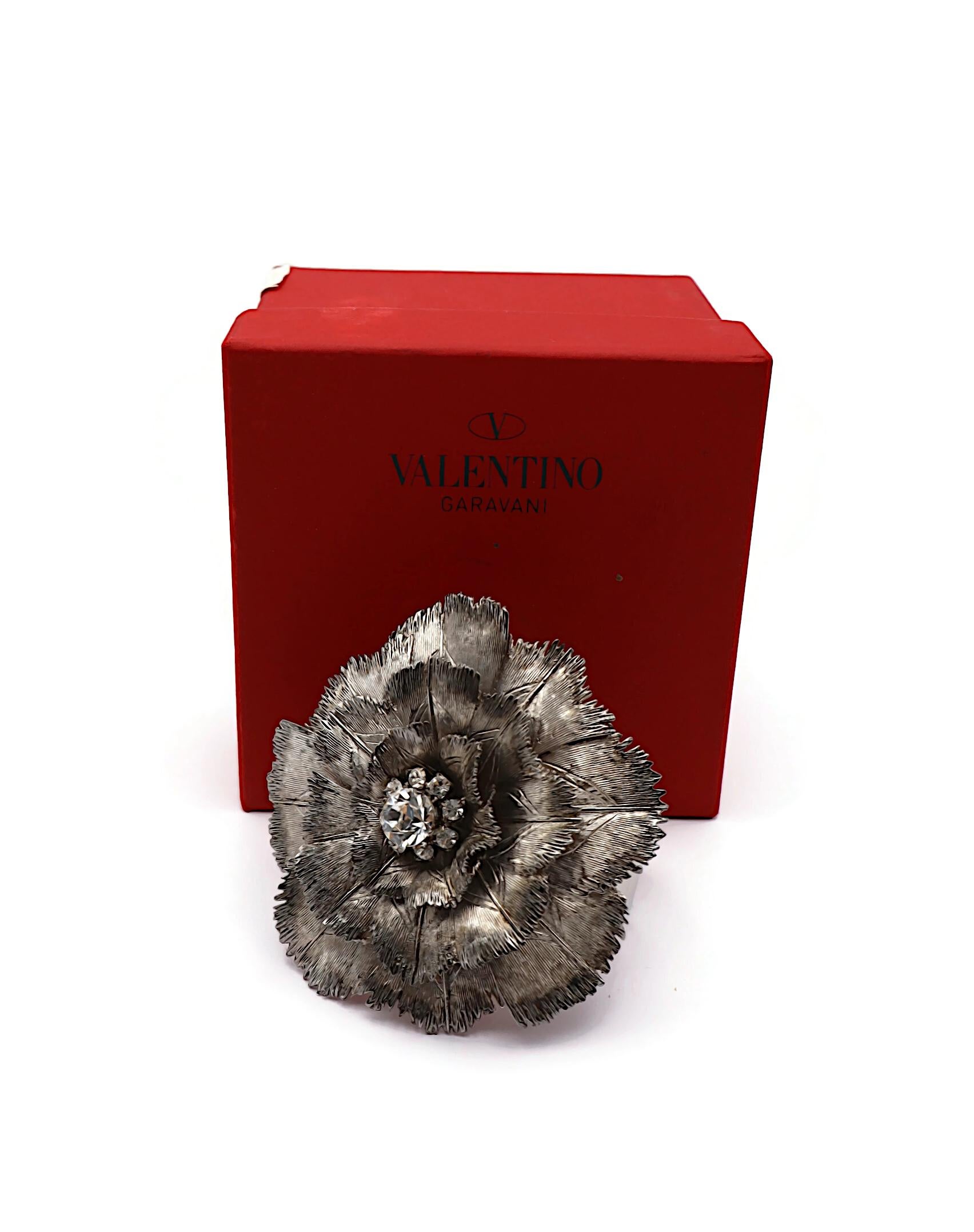 VALENTINO cuff bracelet featuring a large antiqued silver tone flower embellished with clear crystals.

Embossed VALENTINO GARAVANI.
Made in Italy.

Indicative measurements : inner circumference approx. 17.91 cm (7.05 inches) / flower approx. 8.2 x