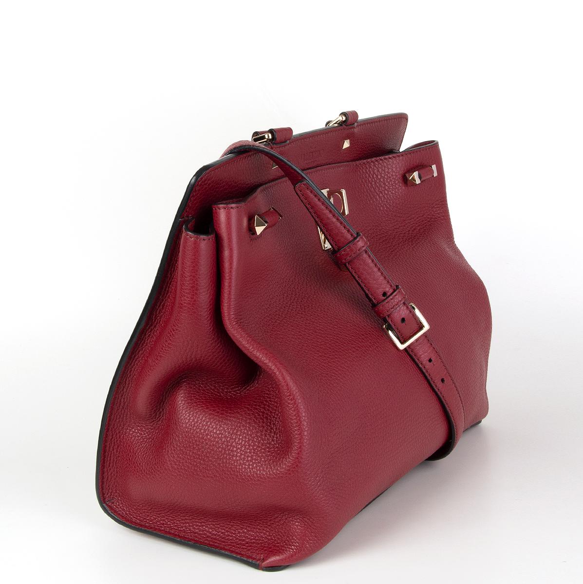 Valentino Garavani 'Joylock' medium top handle shoulder bag in burgundy grained calfskin featuring light gold-tone hardware and lock. Open pocket at the back. The bag can be carried by hand thanks to the top single handle or worn as a shoulder bag