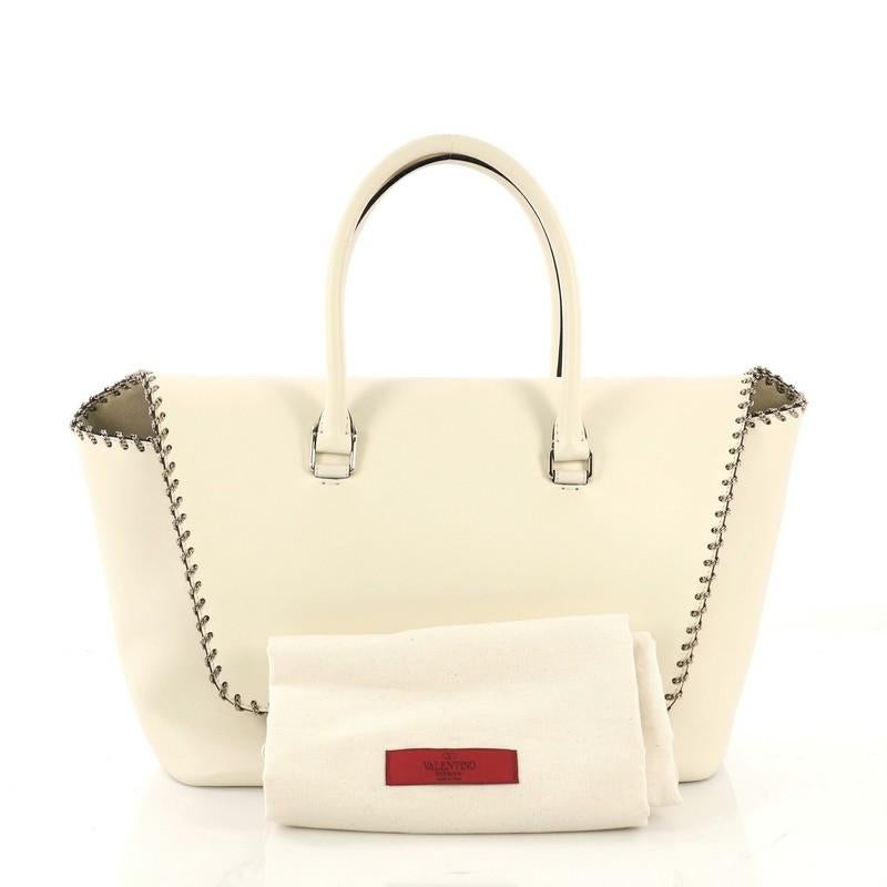 This Valentino Demilune Flap Satchel Leather Medium, crafted in white leather, features dual rolled leather handles, exterior back slip pocket, whipstitch chain trim, and gold-tone hardware. Its flip-lock closure opens to a white microfiber interior