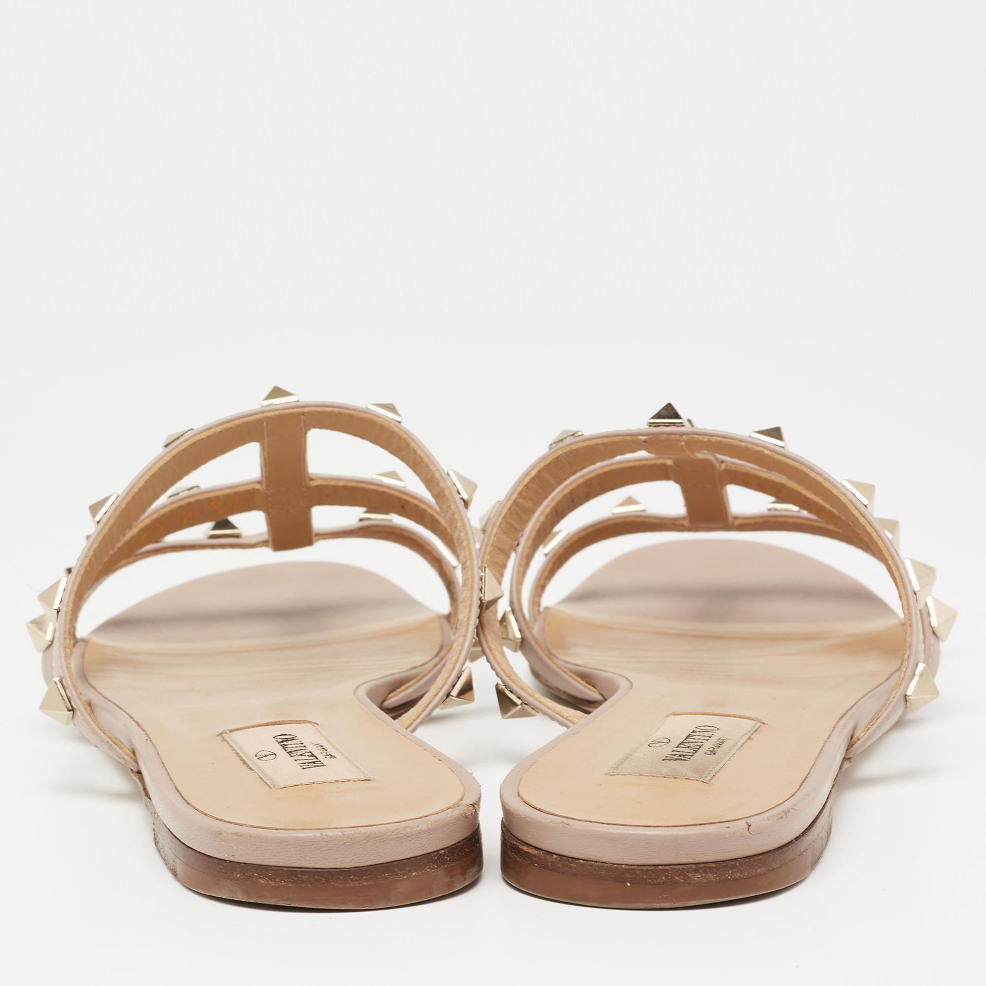 Lend your feet comfort, signature beauty, and luxury with these stunning slide sandals from Valentino. They are crafted using dusty-pink leather, with Rockstud embellishments perched on the upper. They flaunt gold-tone hardware and a slip-on style.
