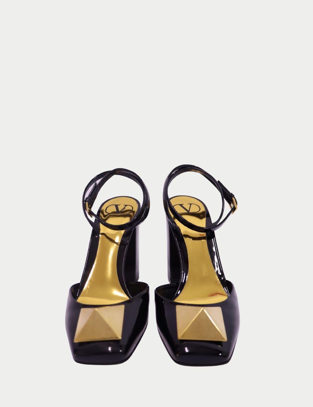 Añade un toque atrevido de lujo italiano a tu vestuario con estos tacones Slingback de charol negro Valentino. Confeccionados en charol negro brillante, estos tacones presentan un llamativo detalle de pirámide dorada en la puntera puntiaguda, que