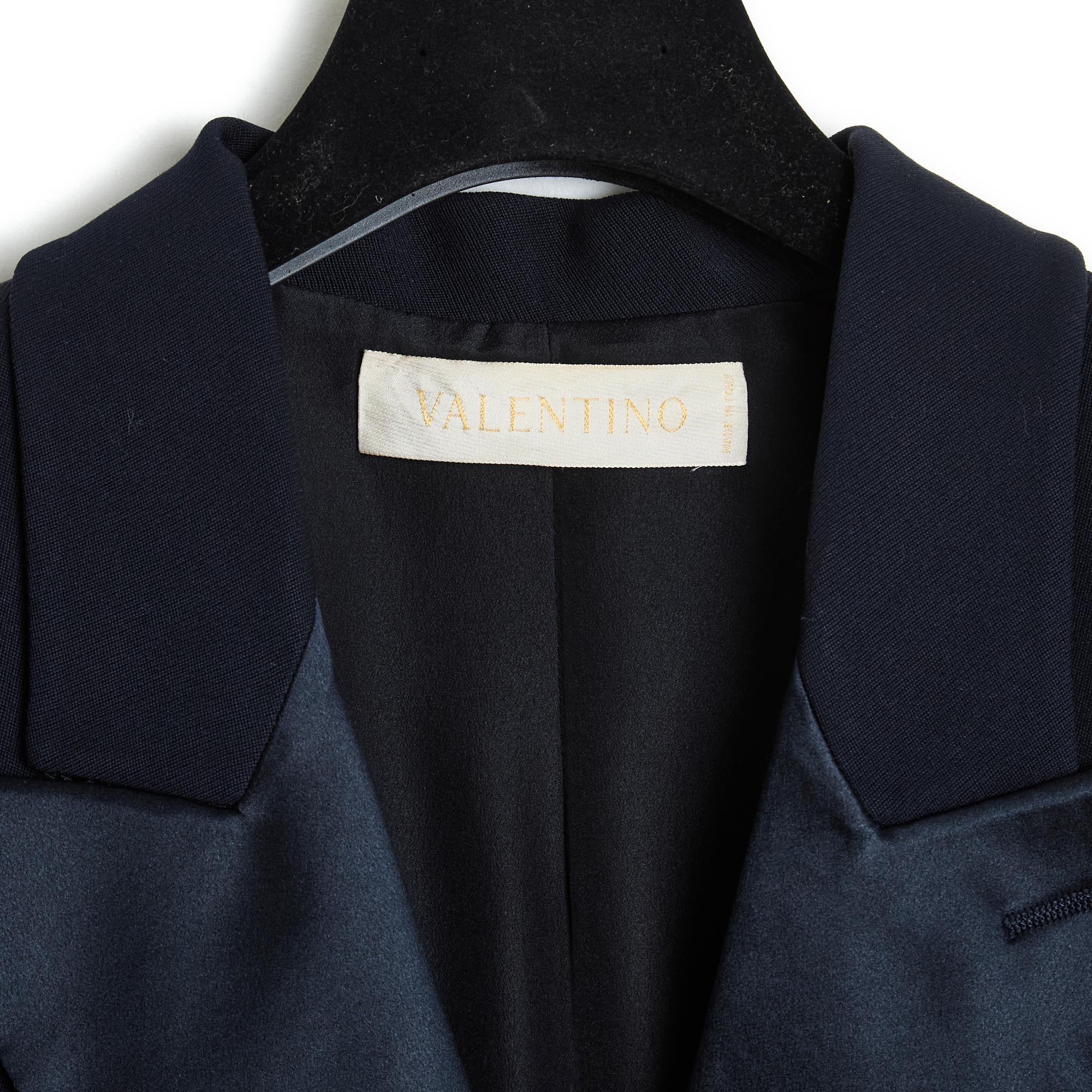 Giacca di Valentino, tailleur pantalone stile smoking, in crepe di lana blu navy e raso di seta coordinato, giacca con colletto dentellato con revers in raso, cintura incrociata sul davanti con 2 bottoni, 2 tasche a fessura sui fianchi, maniche