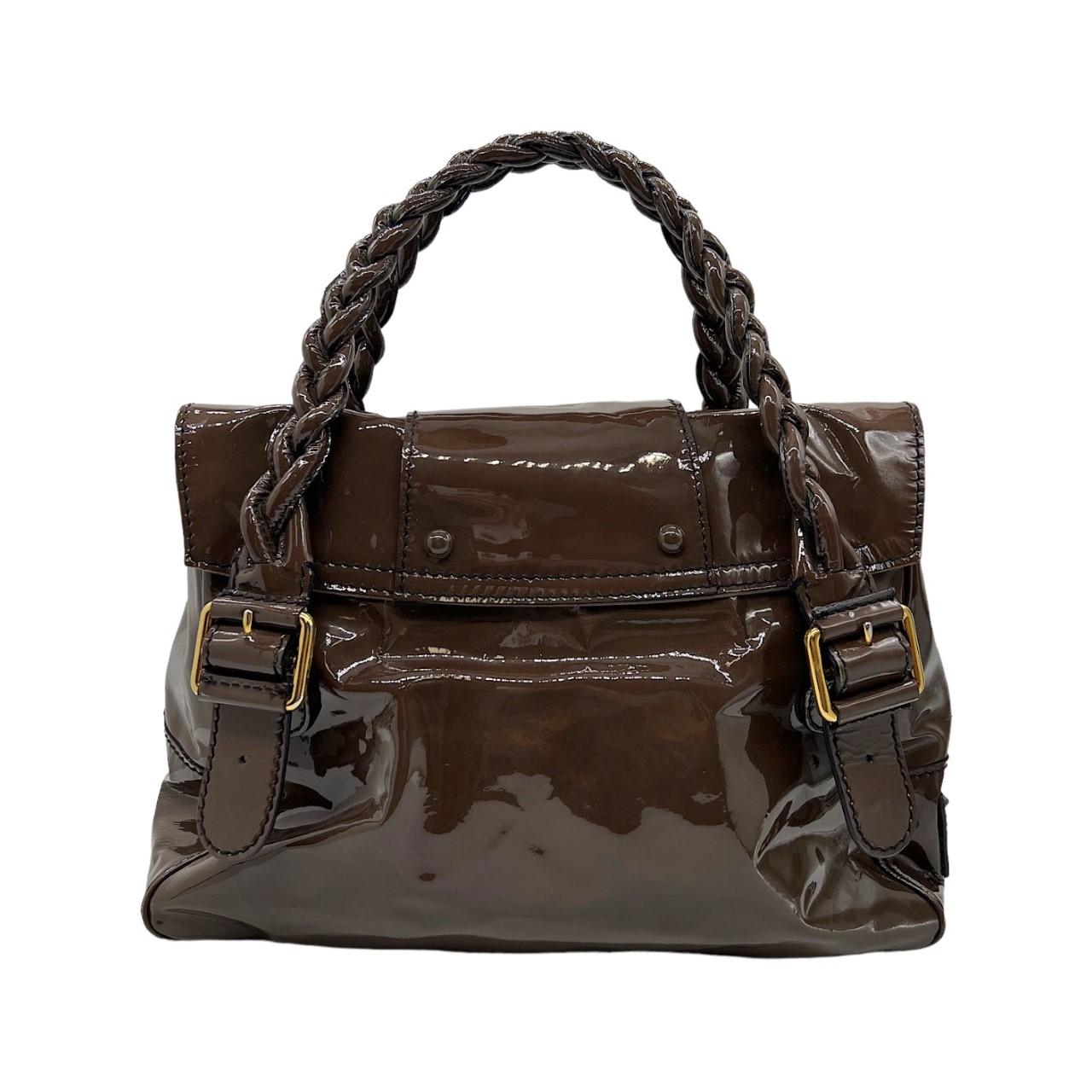 We are offering this stylish Valentino handbag. It is finely crafted of brown patent leather with black contrast stitching around the edges. The bag features braided top handles, frontal pockets, polished brass hardware and a frontal flap. This