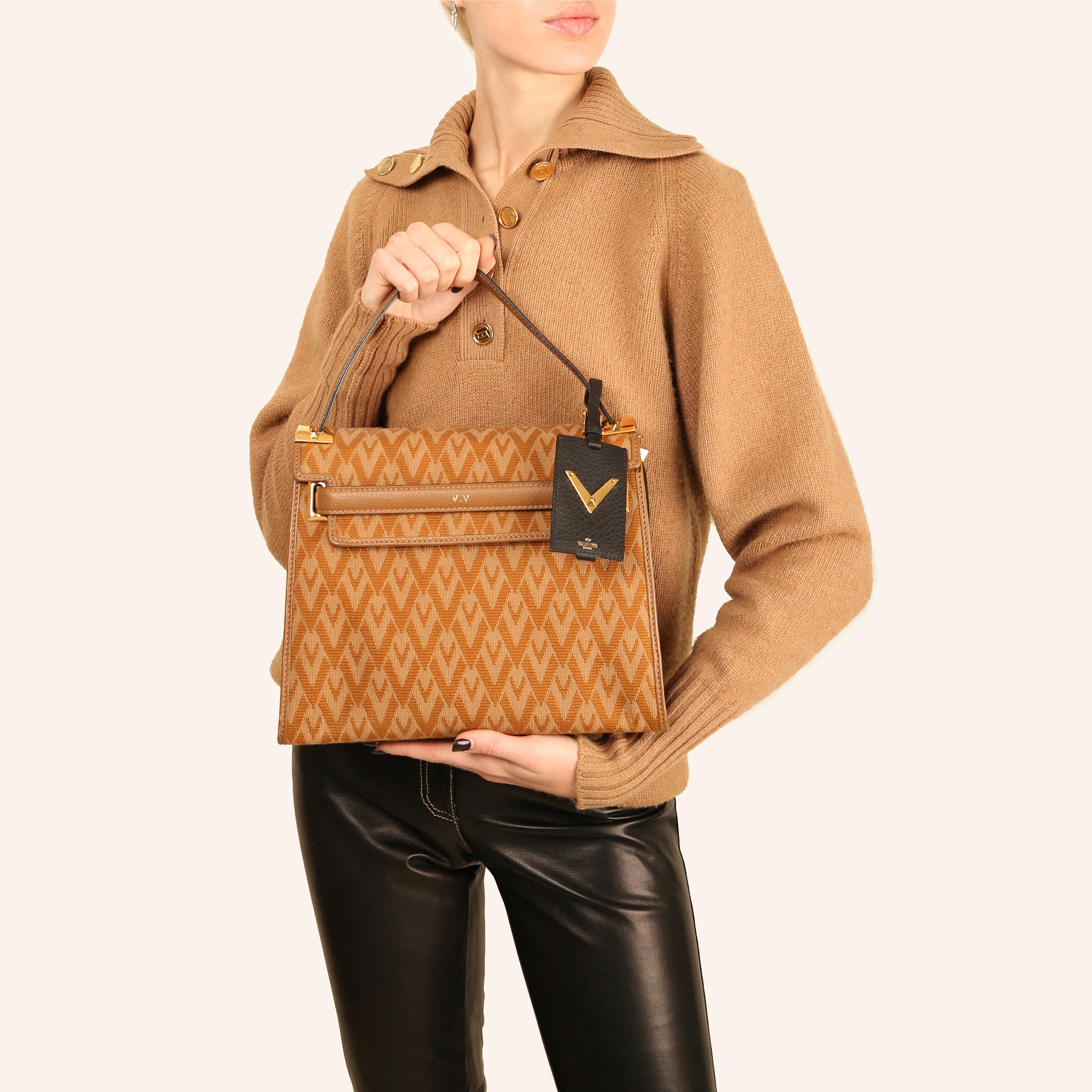 LOVE LALI Vintage

Valentine Garavani trapezoidal style bag crafted in camel fabric that features the V monogram
Finished in camel and black leather with gold stud details and hardware
Front cut out flap
Top handle
Detachable shoulder strap
3 Inner