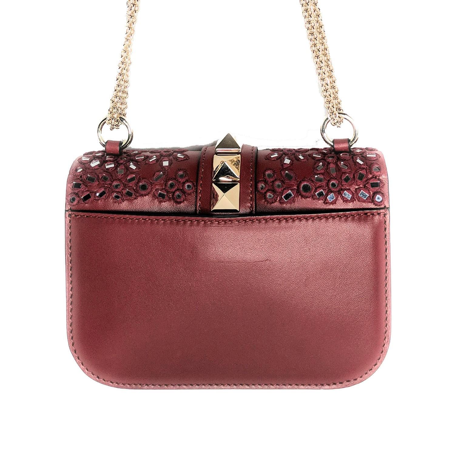 This stylish shoulder bag is crafted of luxuriously smooth lambskin leather in dark red with extensive hand-embroidered floral embellishments with mirror mosaics. The bag features a bijoux gold chain shoulder strap and signature Valentino large gold