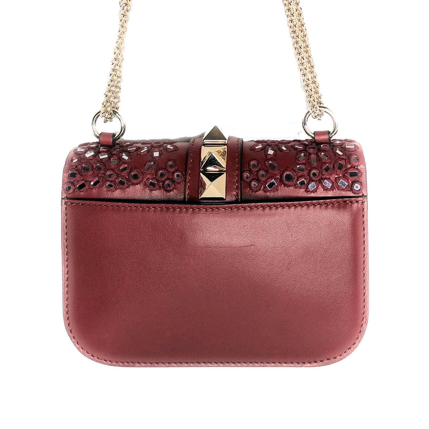Este elegante bolso bandolera está confeccionado en lujosa piel de cordero lisa de color rojo oscuro con amplios adornos florales bordados a mano con mosaicos de espejo. El bolso lleva una bandolera de cadena dorada bijoux y las características
