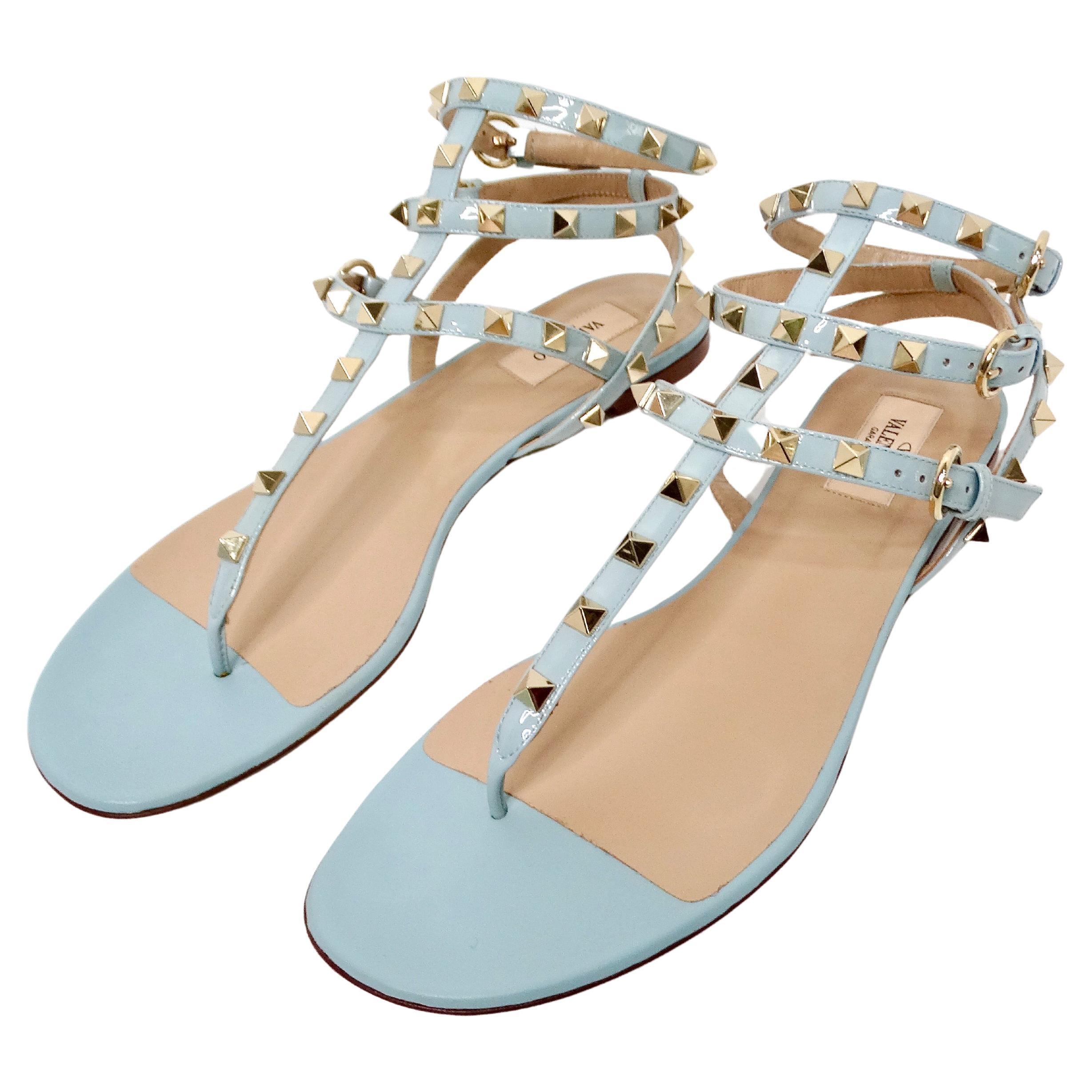 The Valentino Garavani Light Blue Rockstud Flat Patent Leather Sandals exemplify sophisticated elegance with an edgy twist. Crafted from sleek patent leather in a stunning light blue hue, these sandals feature the iconic Rockstud detailing along the