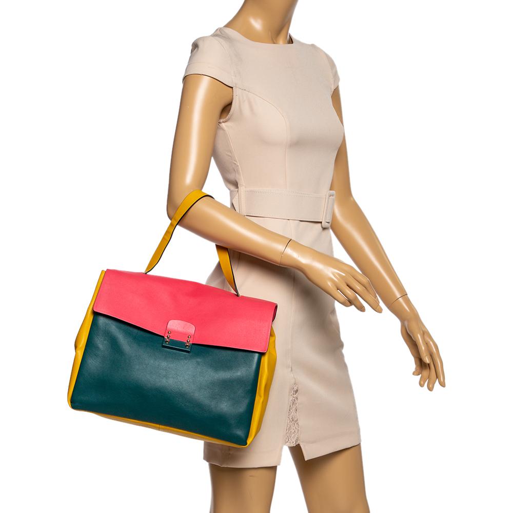 This Valentino beauty is crafted in Italy and made from quality leather. It is designed with a color blocking pattern. The top handle bag features a front flap that is secured by a gold-tone lock. The creation comes with a well-sized leather