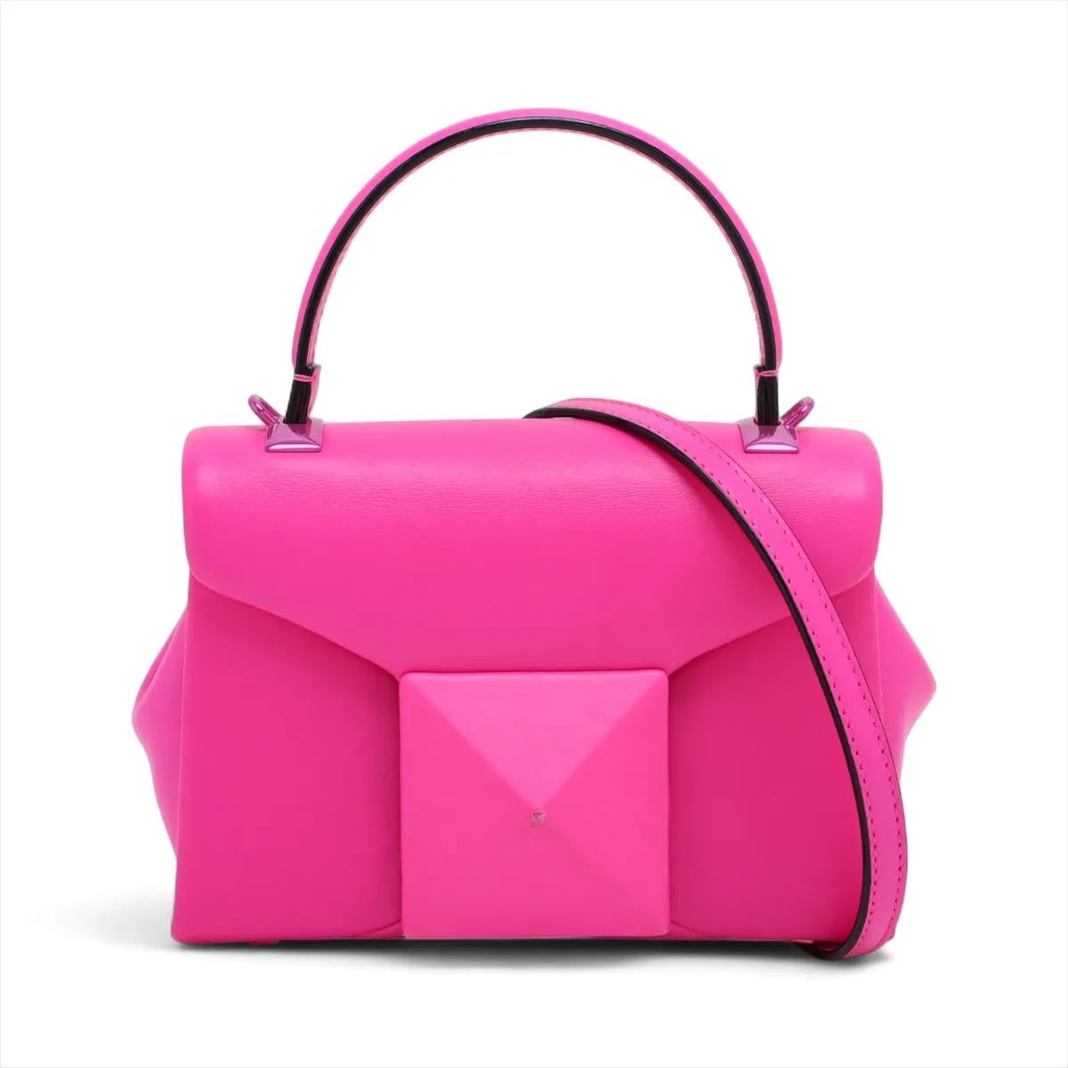 Le sac à main Valentino Garavani One Stud Two-Way en rose est une déclaration d'élégance moderne et de savoir-faire raffiné. Confectionné en cuir lisse et luxueux, il arbore le clou pyramidal surdimensionné signature de la marque, emblème audacieux