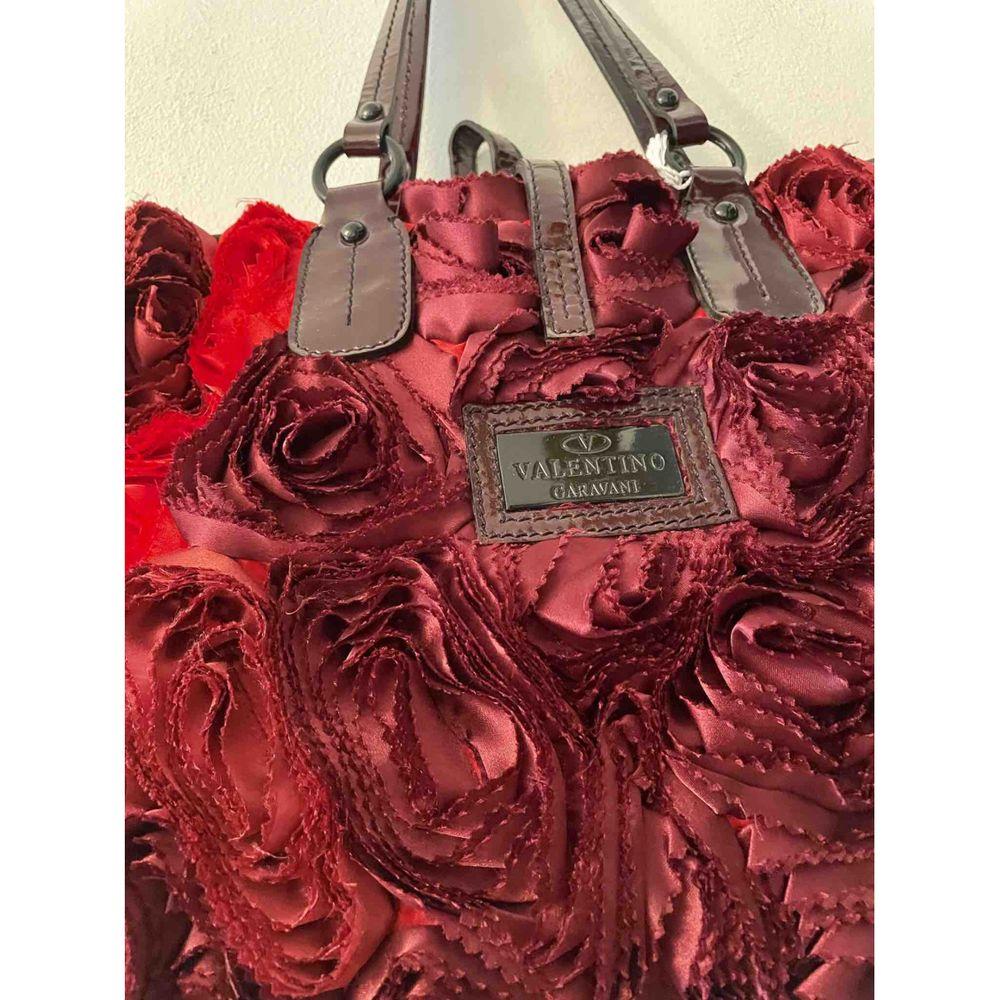 Valentino Garavani Patent Leather Handbag in Burgundy

Valentino Garavani bag in burgundy patent leather and entirely covered with burgundy and red silk roses. Closure with laces and two rings. Roomy interior with side pocket closed with zip. It has