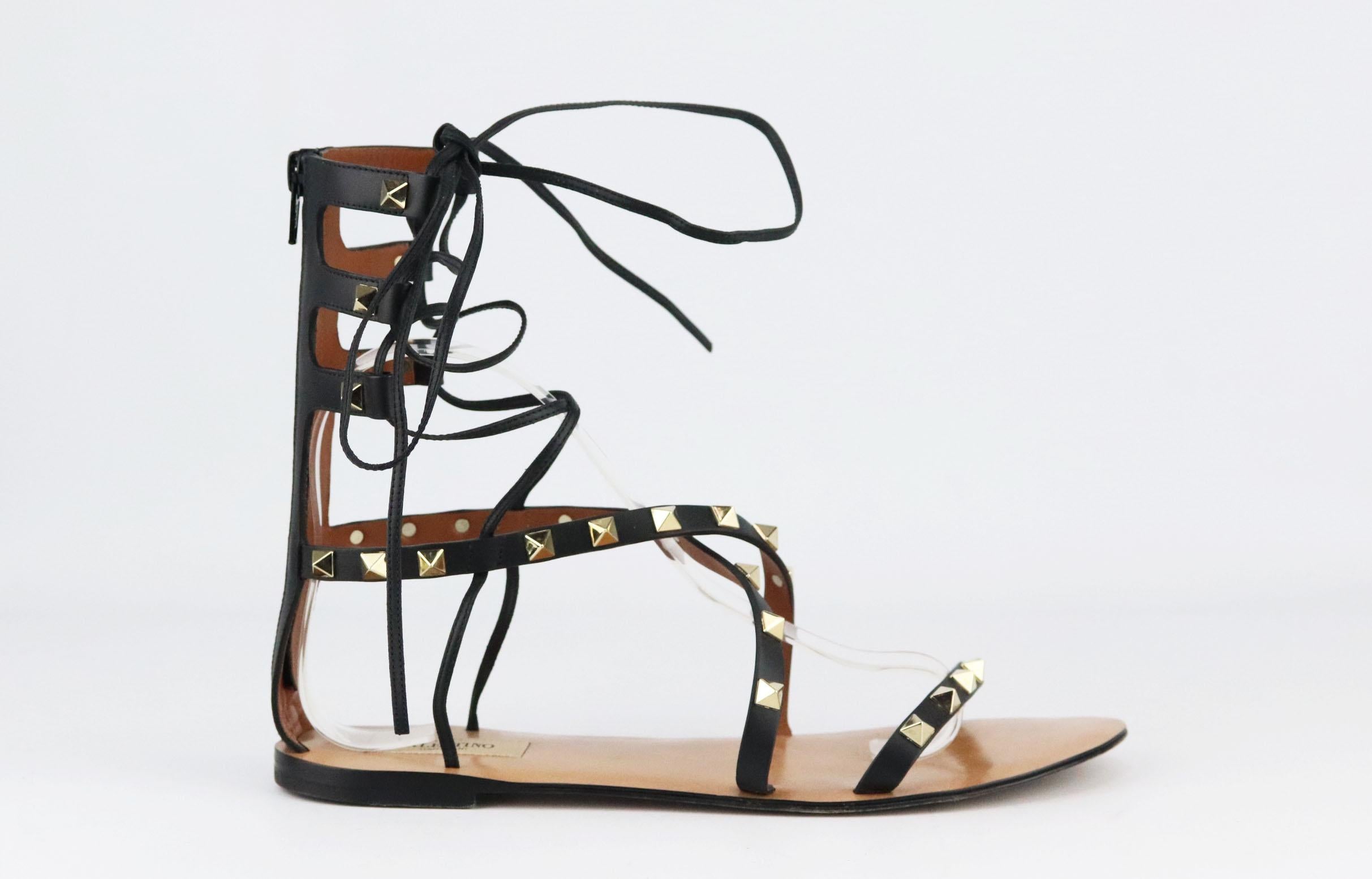 Crafted from supple black leather, Valentino Garavani's sandals are adorned with the brand's signature gold pyramid studs; this pair has flattering cross-over straps and gladiator-inspired laces. 
Sole measures approximately 10 mm/ 0.4 inches.